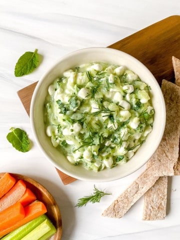 cottage cheese tzatziki in a cream bowl on a wooden chopping board.