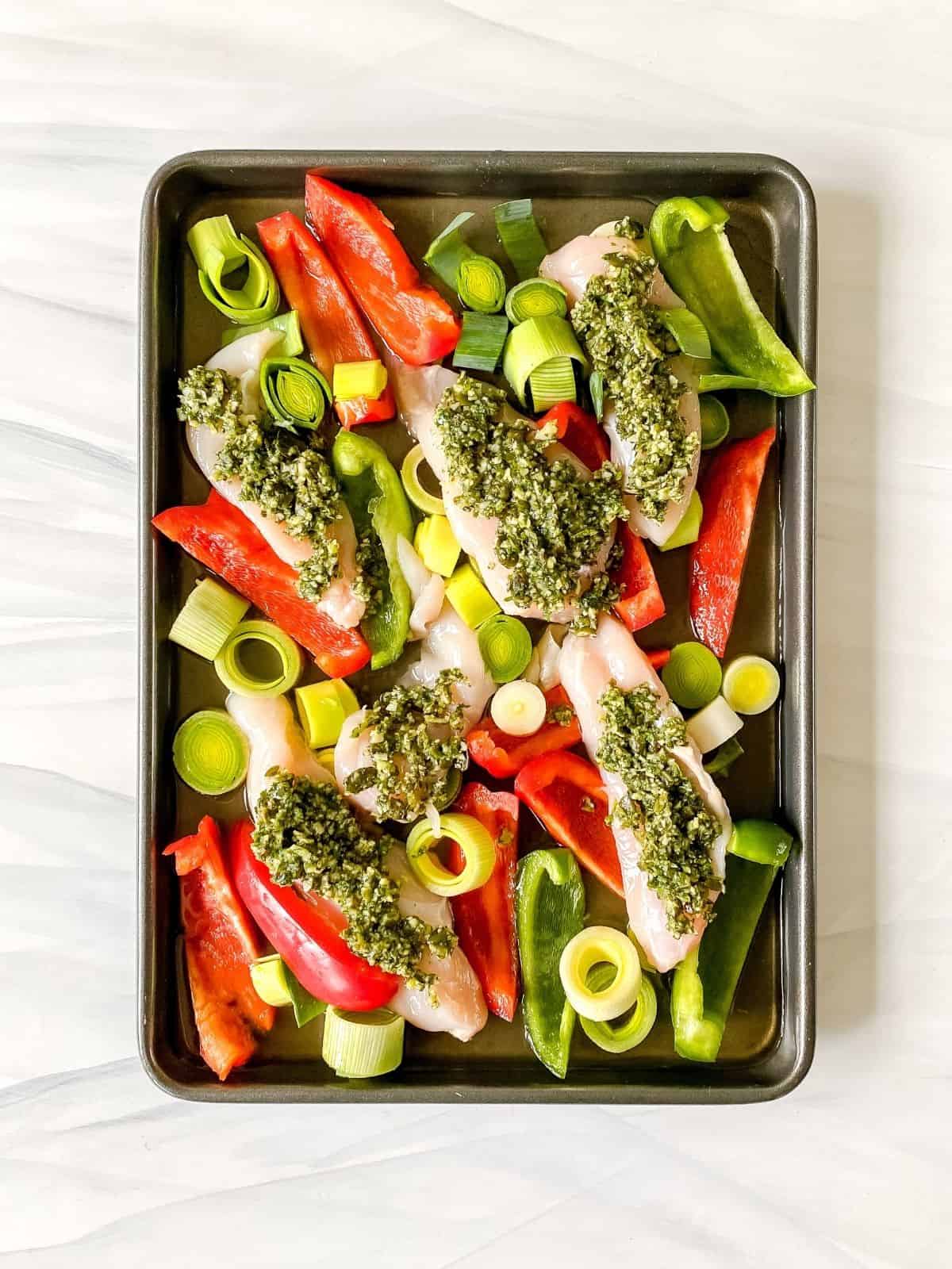 vegetables and pesto coated chicken breasts on a baking tray.
