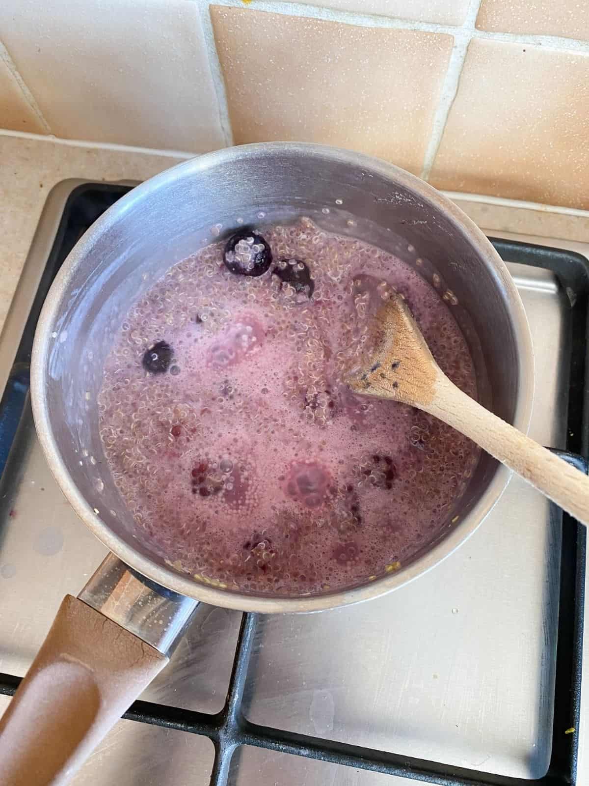 blackberry quinoa porridge cooking in a pan on a stove top.
