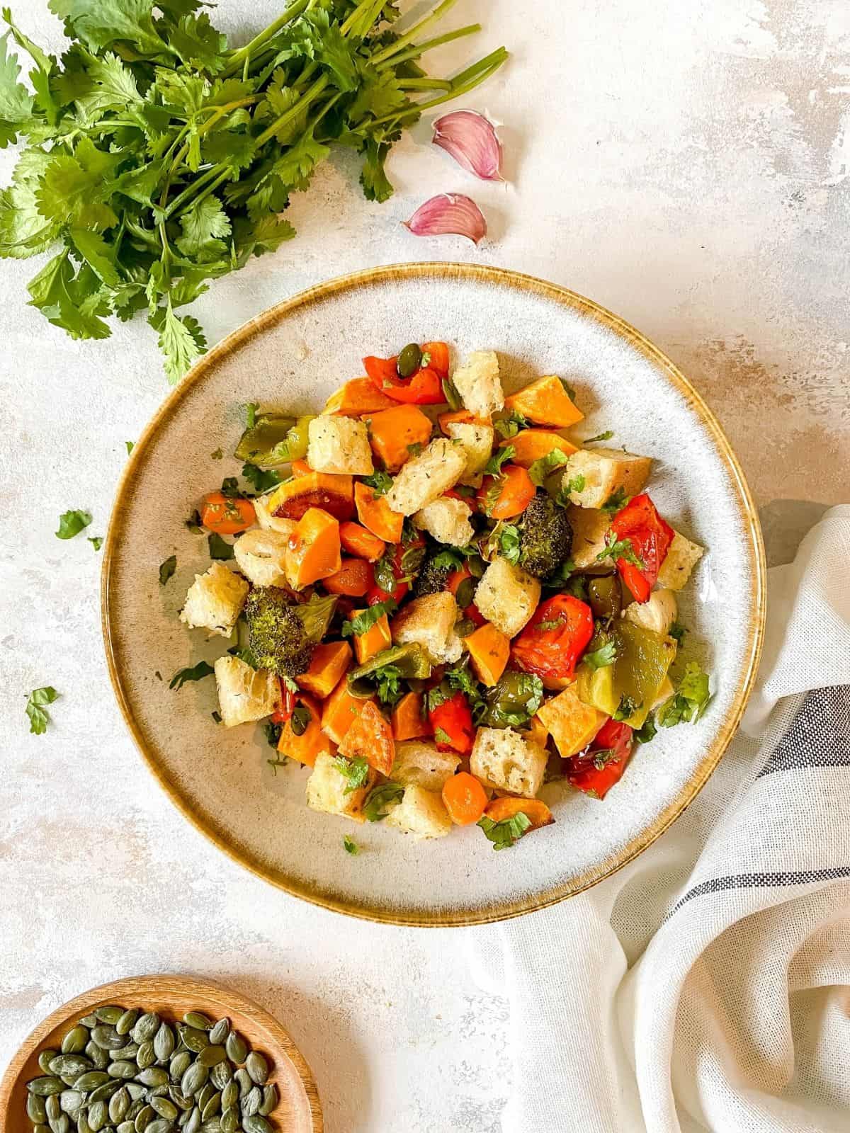 roasted vegetable panzanella in a grey bowl with herbs next to it.