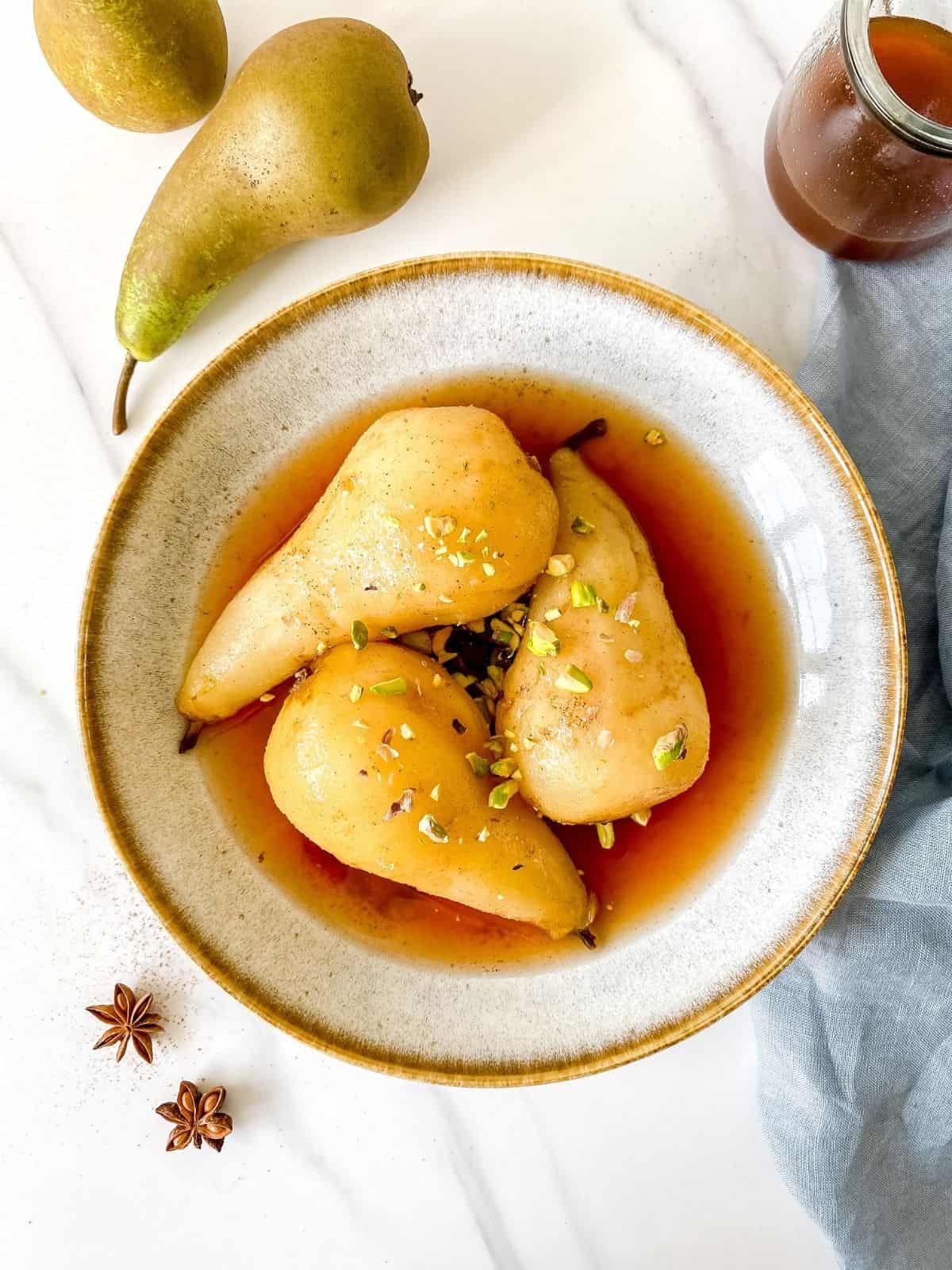 spiced poached pears in a light grey bowl on a blue cloth next to star anise.