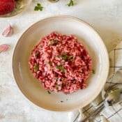 beetroot risotto in a brown bowl with spoons on a tea towel next to it.