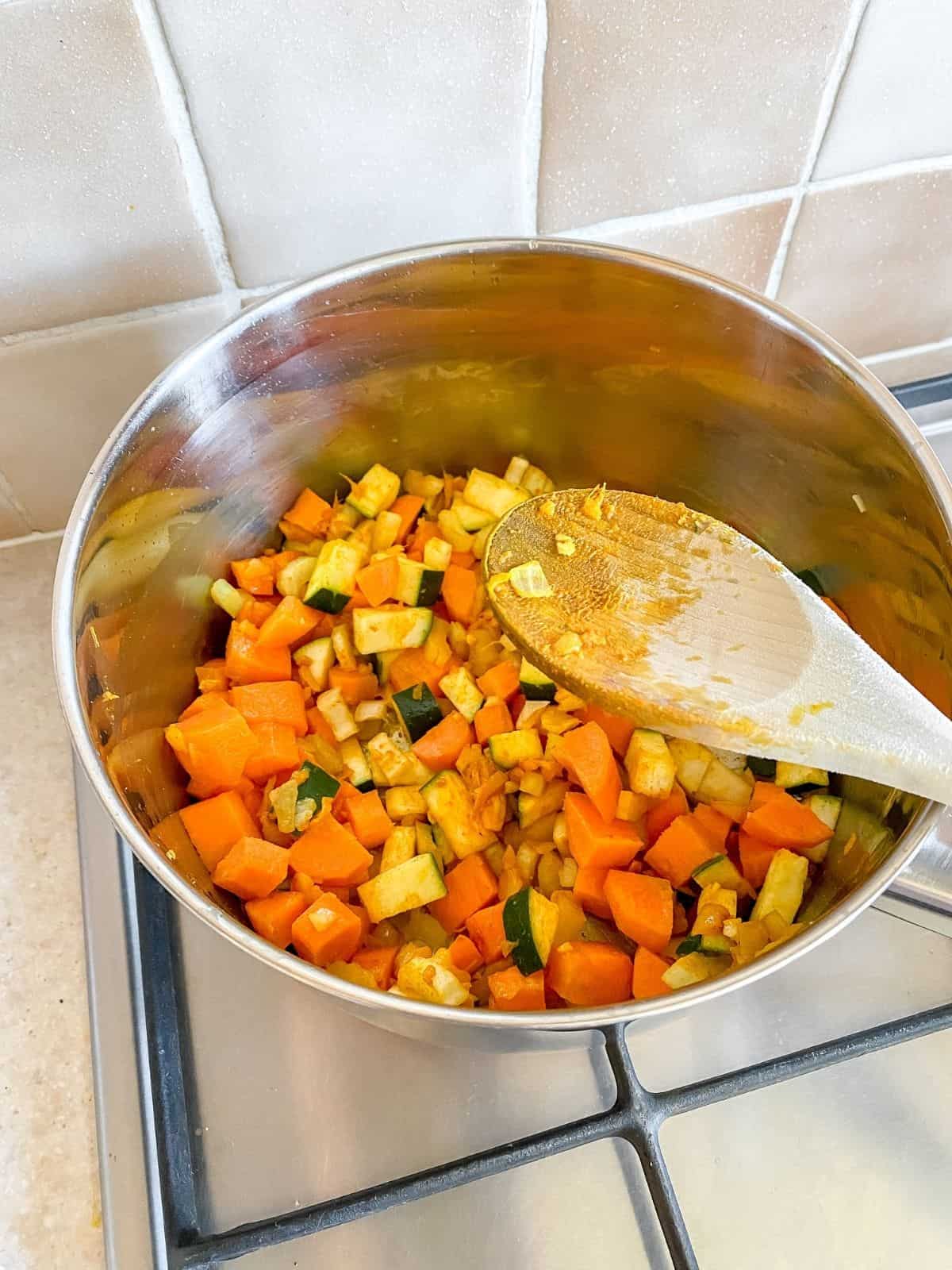vegetables in a pan on a stove top with a wooden spoon on it.