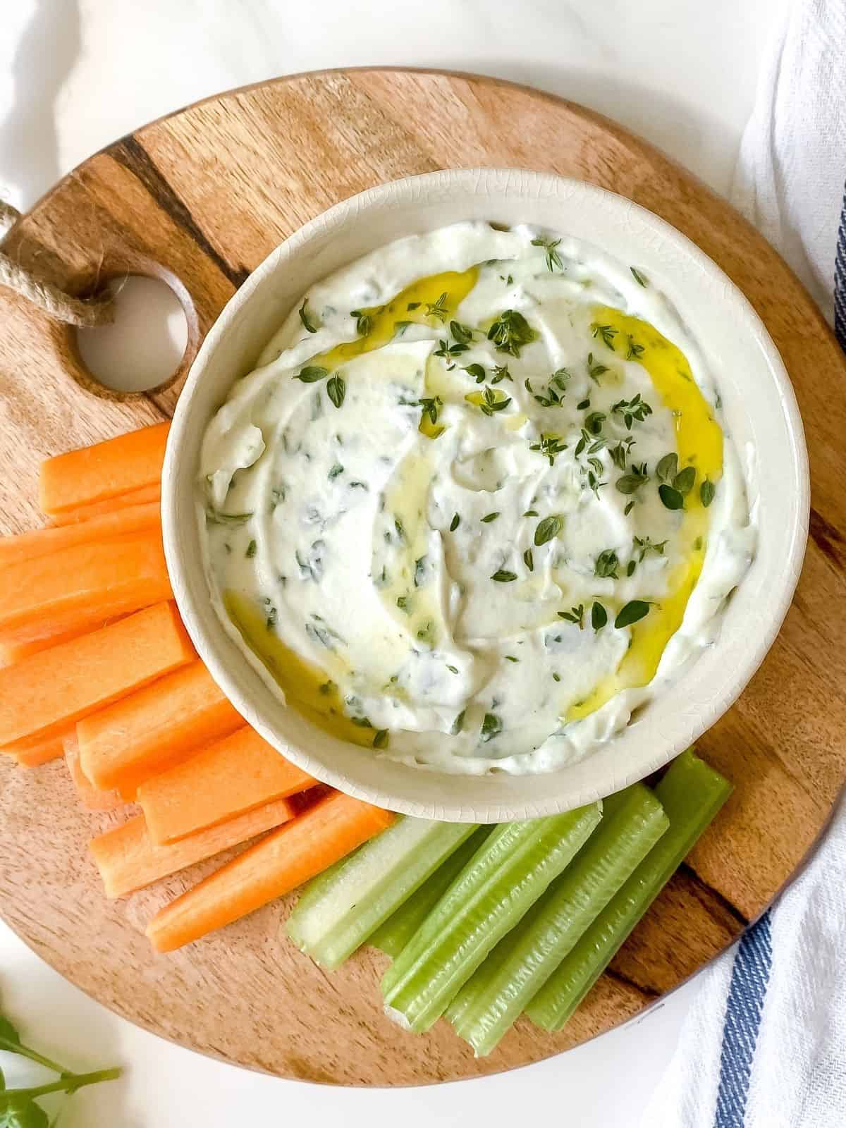 whipped ricotta dip with honey and herbs on a chopping board with carrots and celery.