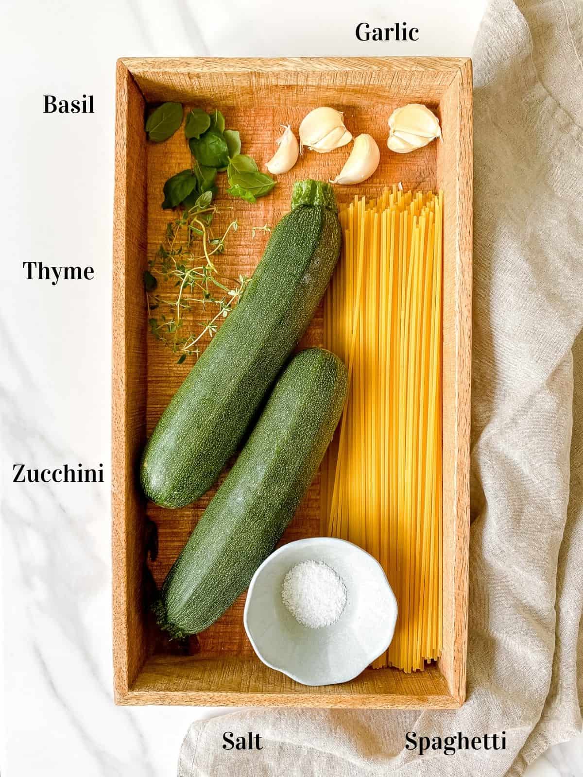 wooden box with zucchini, spaghetti, salt, garlic, basil and thyme in it.