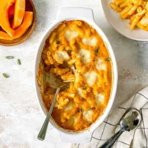 butternut squash pasta bake in a white dish with a spoon in it next to a plate of pasta bake.