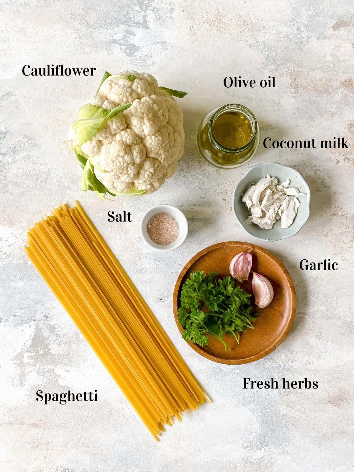 overhead view of individually labelled cauliflower, olive oil, coconut milk, salt, spaghetti, fresh herbs and garlic.
