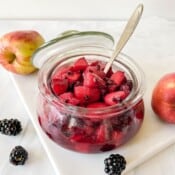 apple and blackberry compote in a glass jar with a spoon in it.