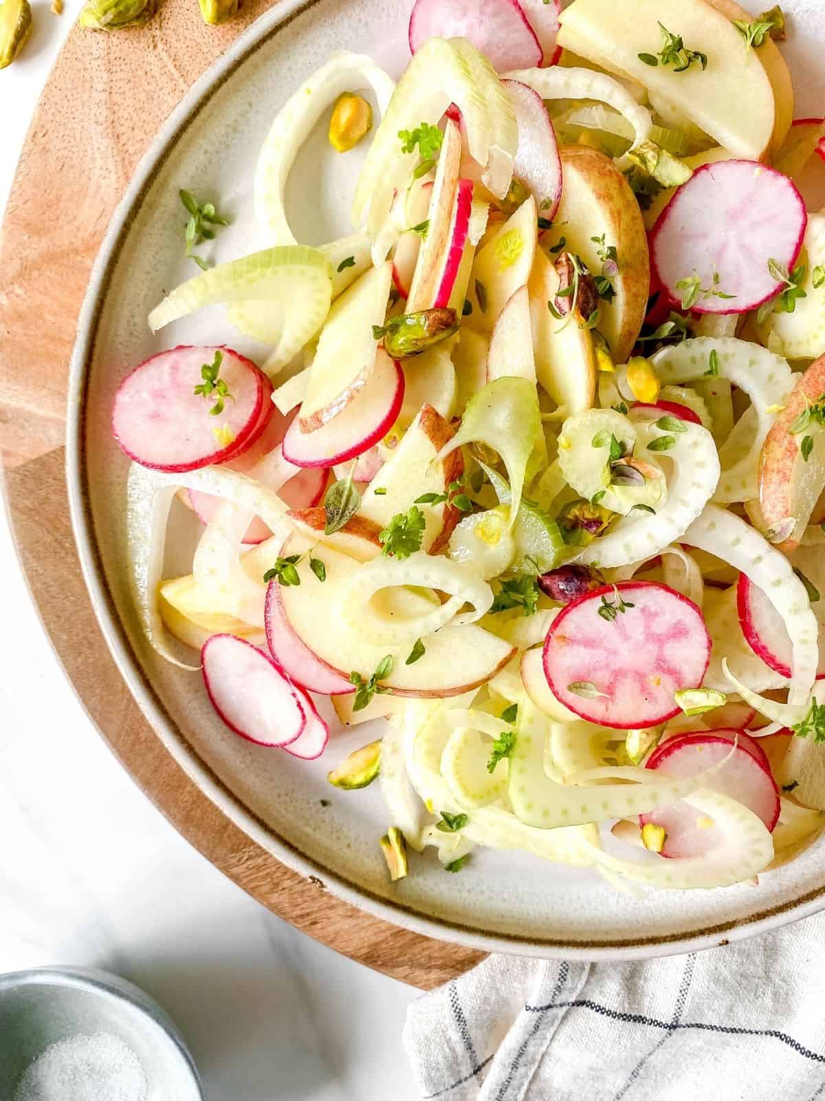 apple, fennel and radish salad on a brown plate on a wooden board.