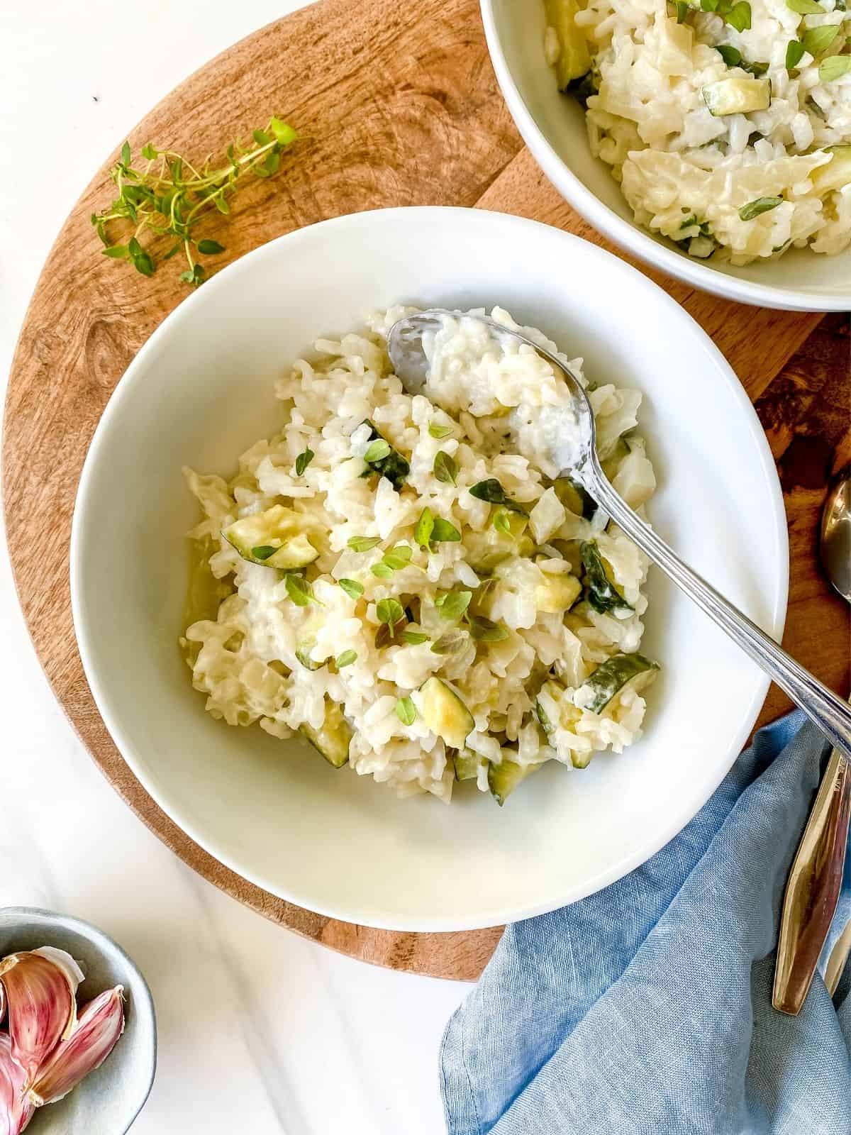 two bowls of baked fennel risotto on a wooden board with spoons in them.