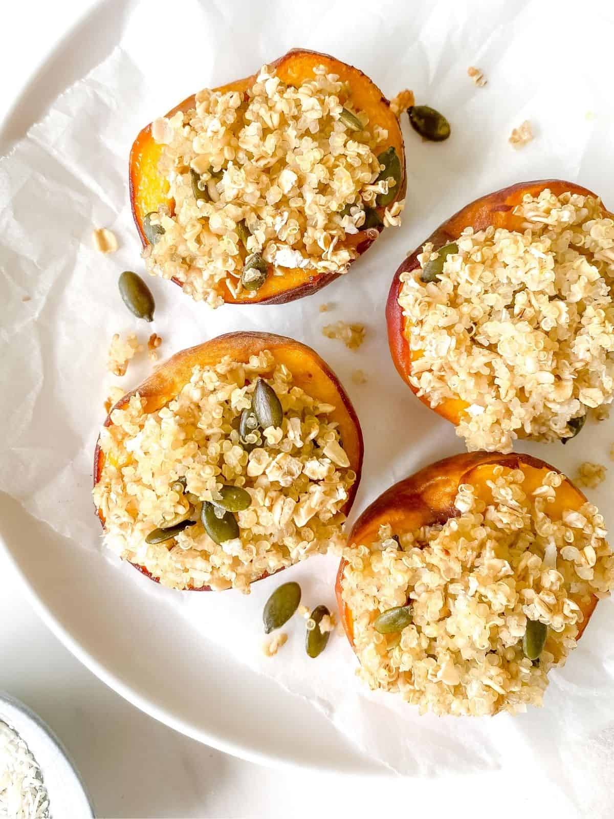 four baked peaches with a crumble topping on a white plate.