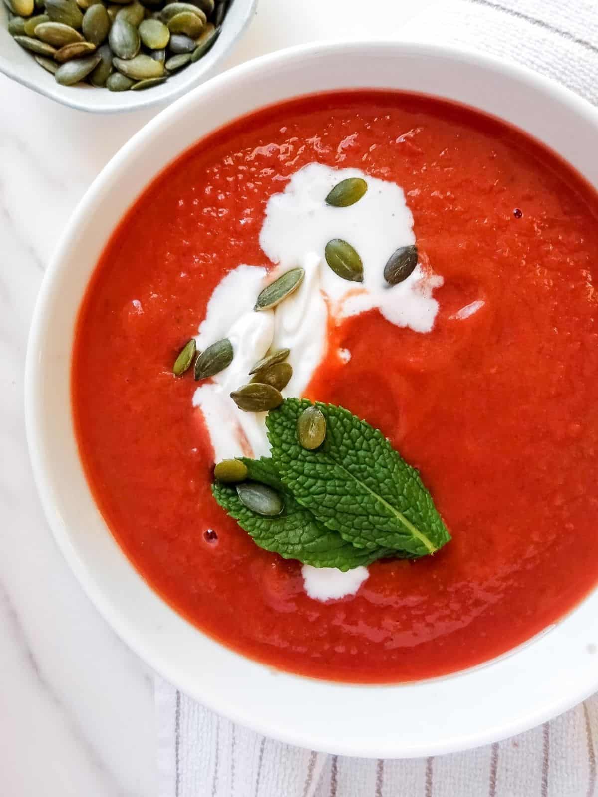 beetroot and sweet potato soup in a white bowl garnished with mint and coconut cream.