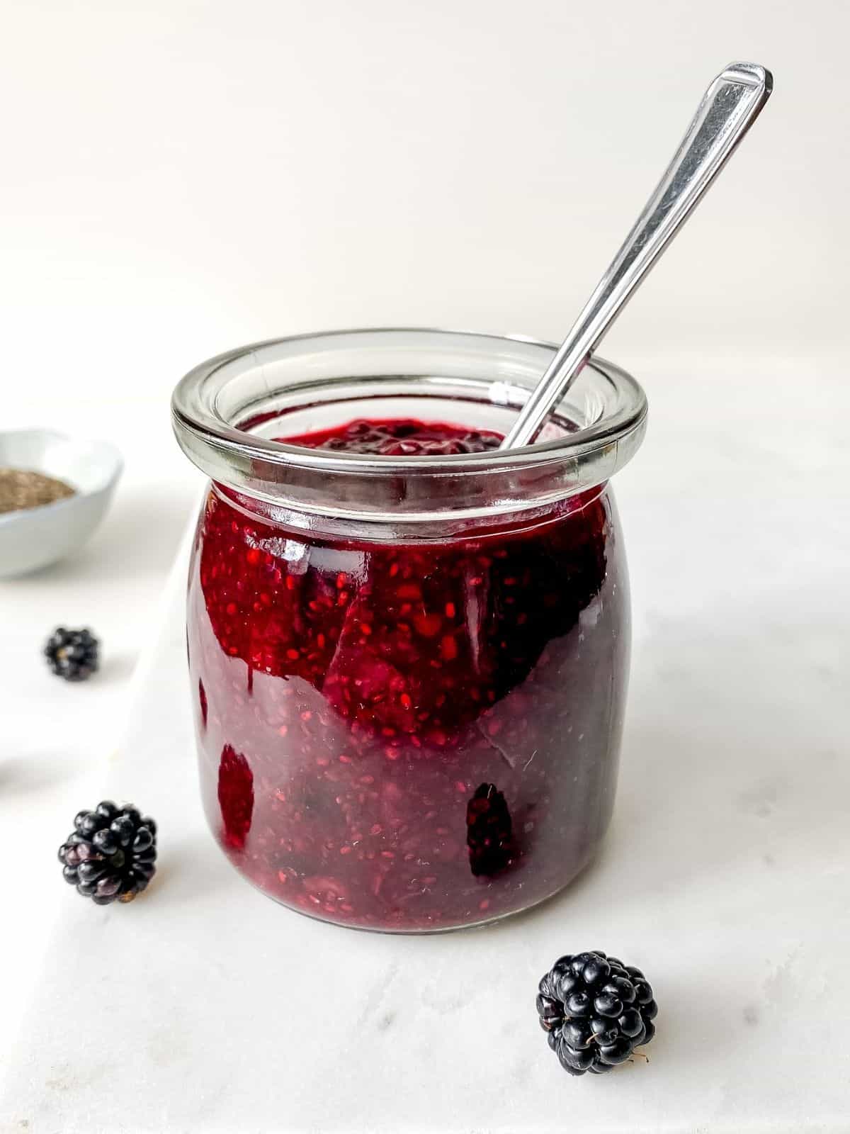 glass jar or blackberry chia jam with a blue bowl of chia in the background.