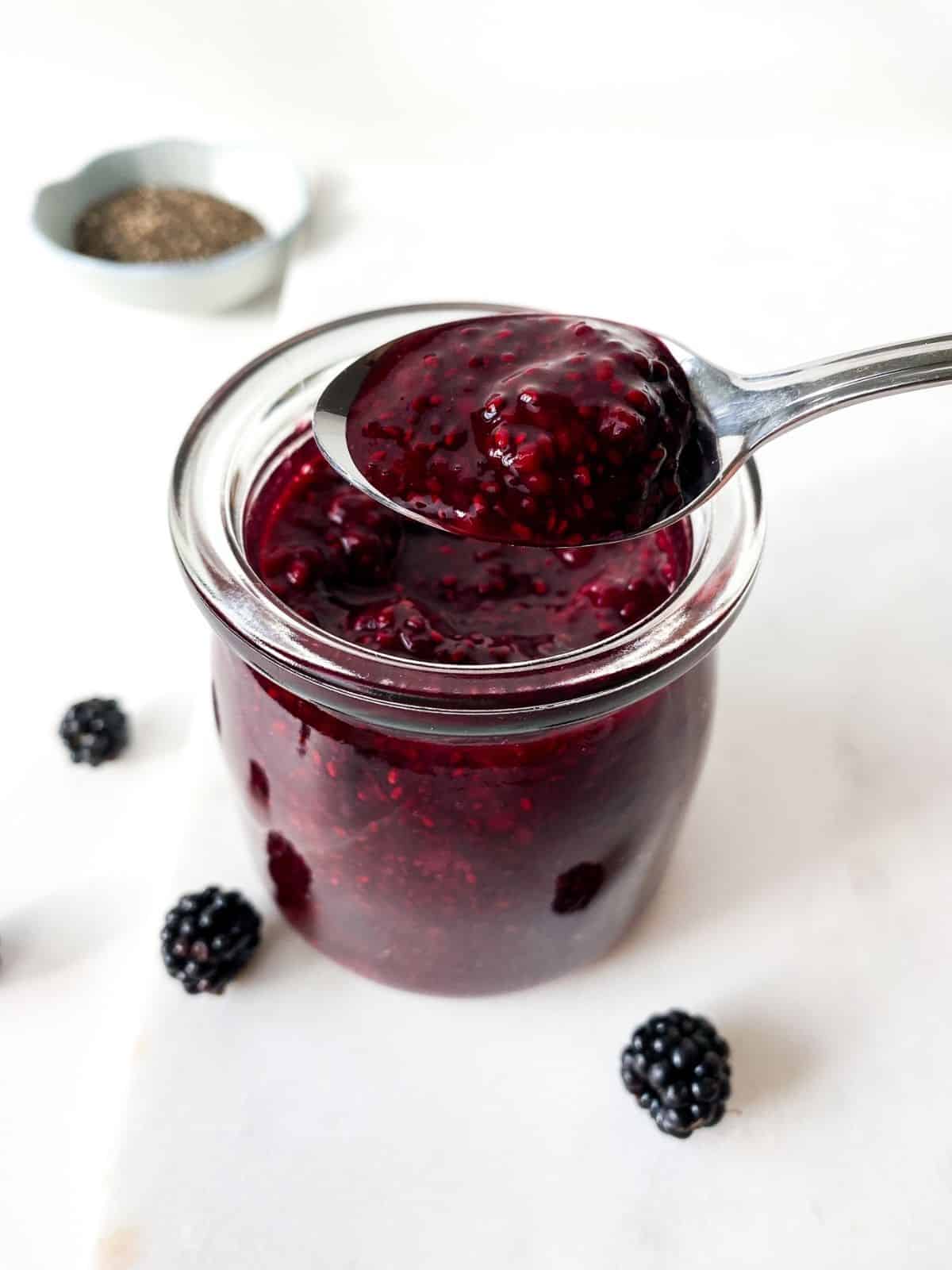 glass jar of blackberry chia jam with a spoonful of jam above it.