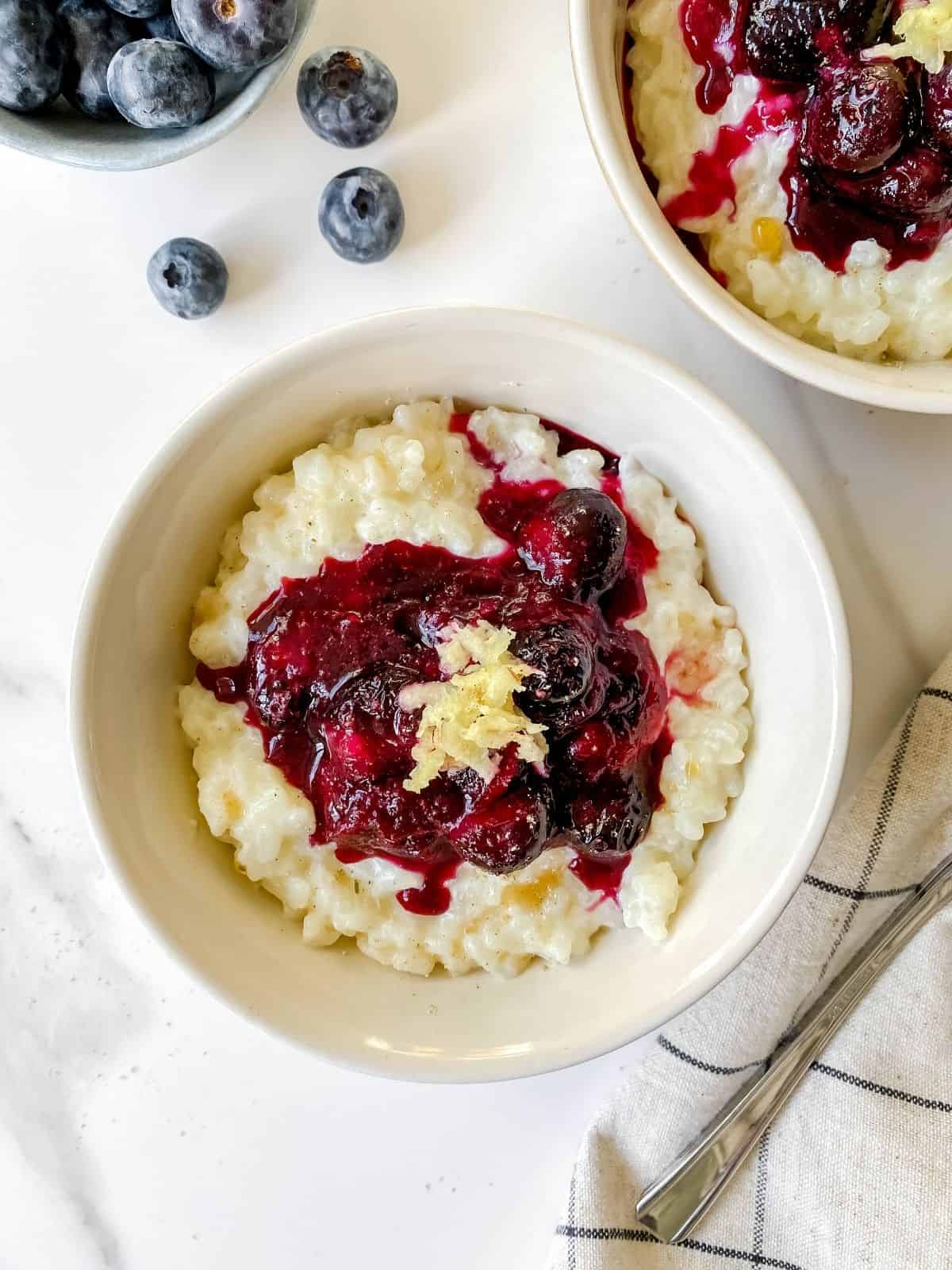 blueberry rice pudding in two white bowls on a checked cloth.