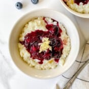white bowl of blueberry rice pudding on a checked cloth.