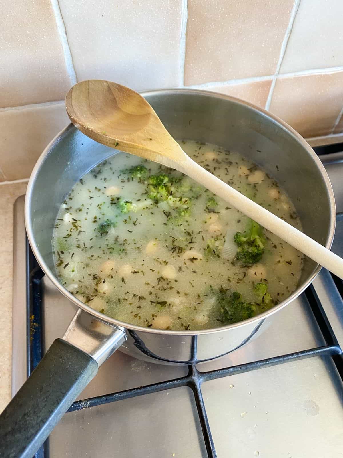 broccoli, cauliflower and coconut milk in a pan with a spoon on it.