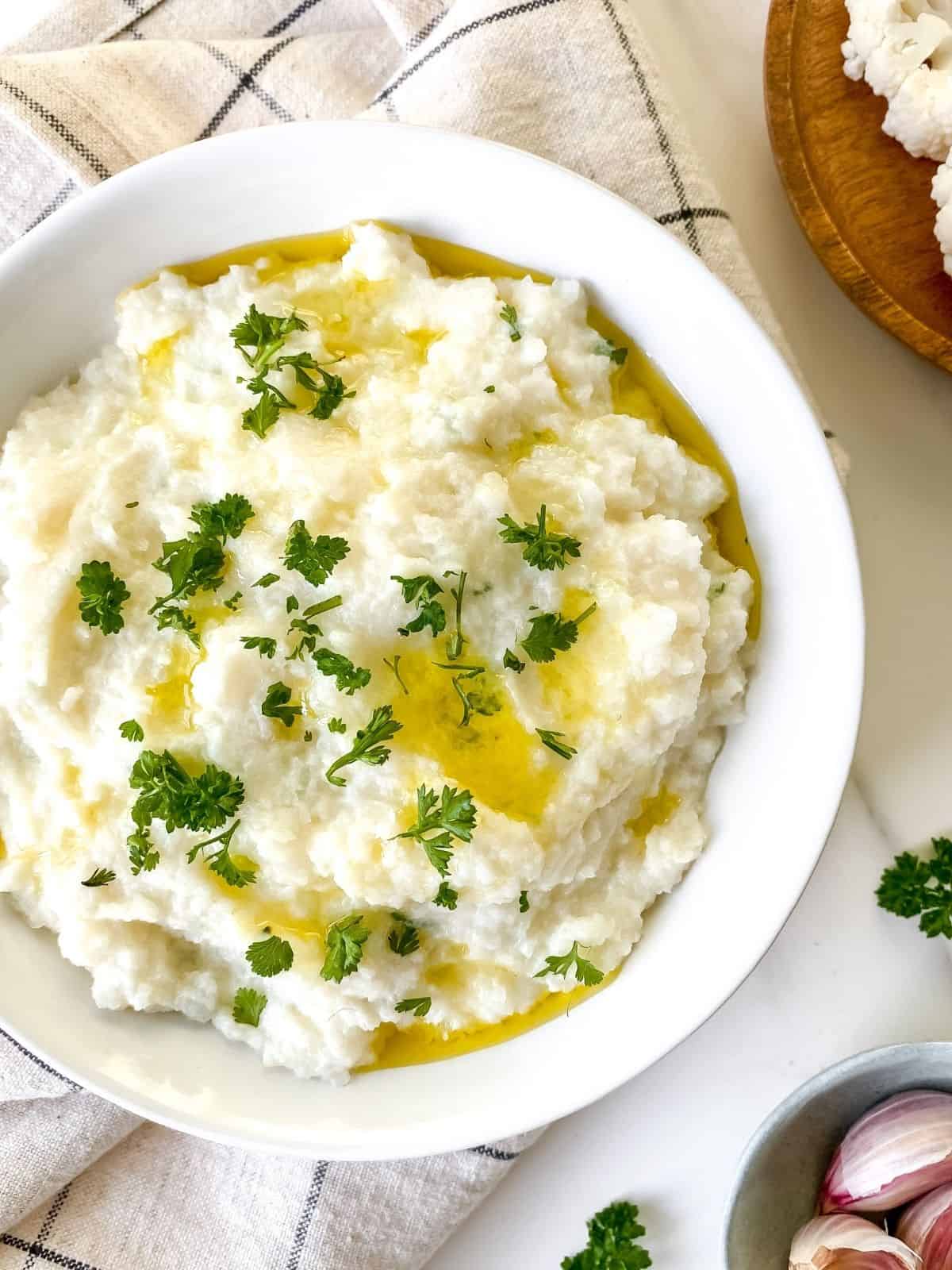mashed cauliflower with cream cheese in a white bowl on a cream checked cloth.
