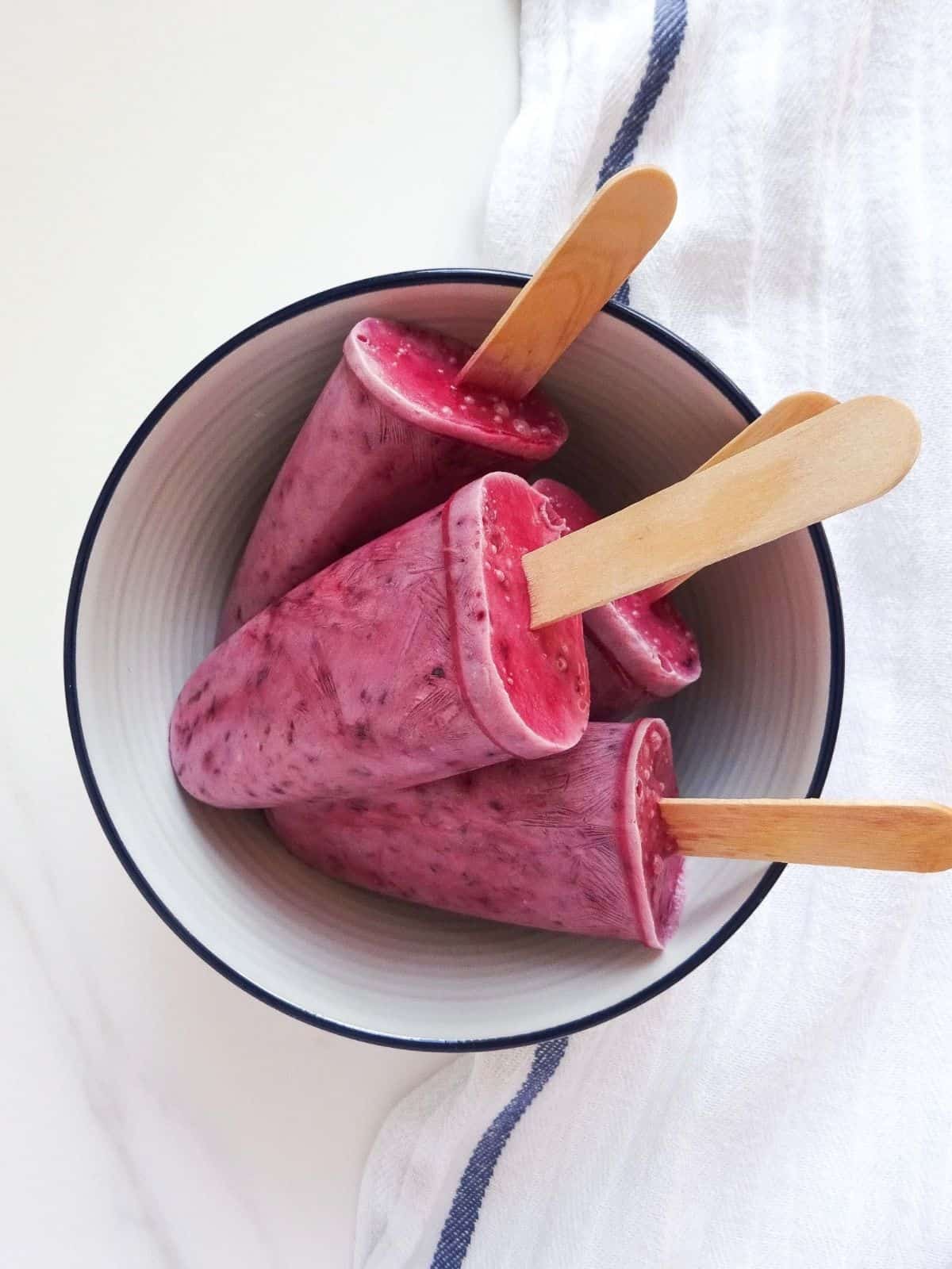 cherry coconut popsicles in a white bowl with a blue rim.