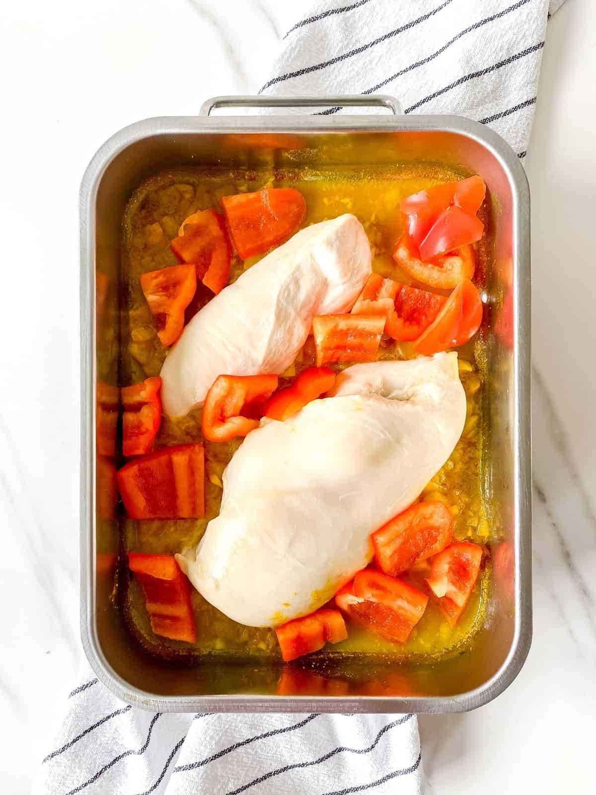 chicken thighs and red bell pepper in a metal dish.