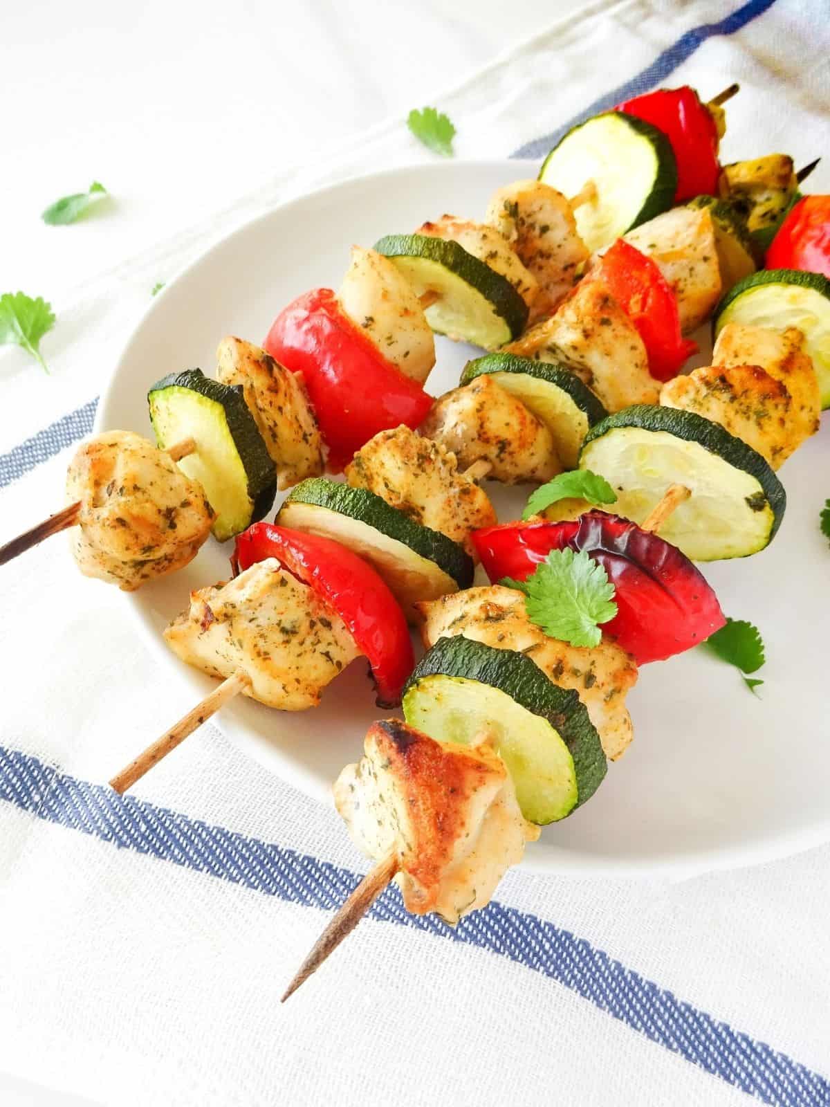 a white plate with coconut chicken skewers on top of a blue and white striped cloth.