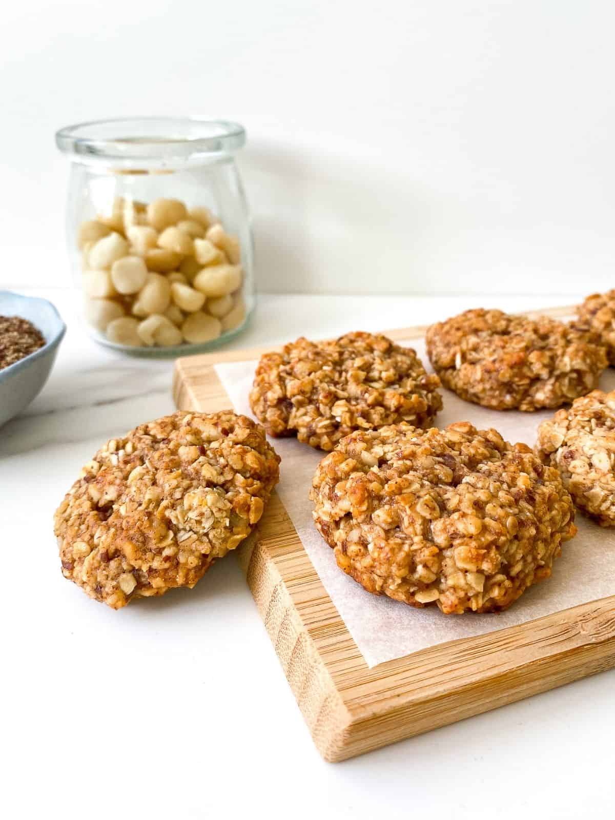 wooden board with coconut macadamia nut oat cookies on it, with a jar of nuts in the background.