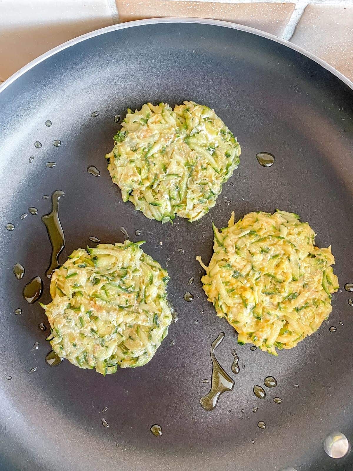 zucchini fritters being fried in a pan.
