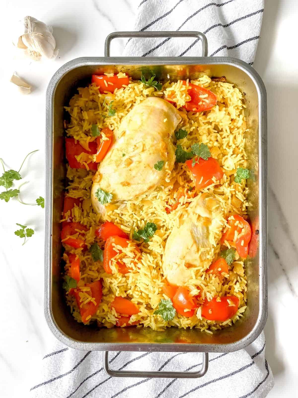 ginger chicken pilaf traybake in a metal dish on a striped cloth.