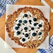 granola breakfast pizza on a wooden board on a blue cloth.