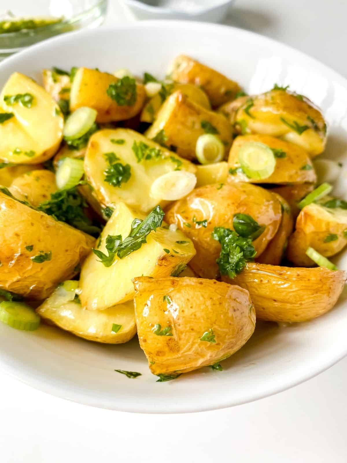 close up of a white bowl of herbed roasted potato salad.
