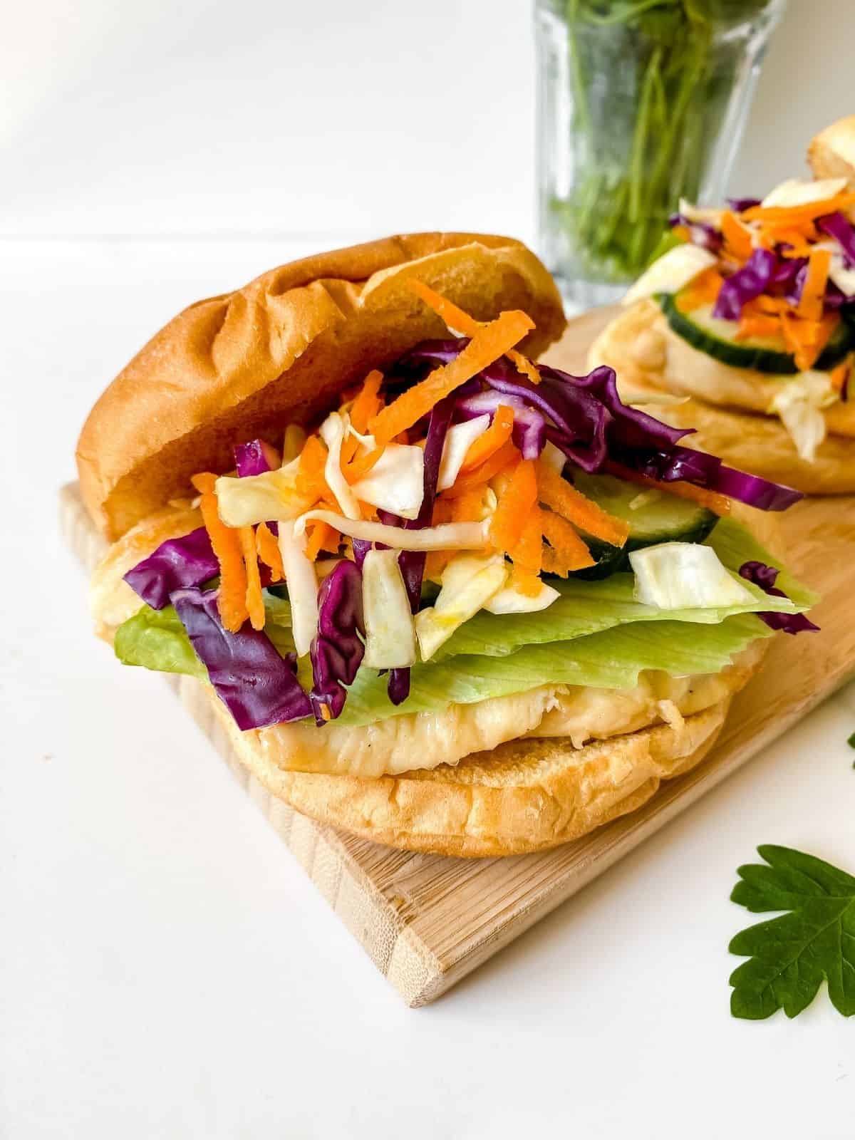 honey chicken burger in a bun with slaw on a wooden board.