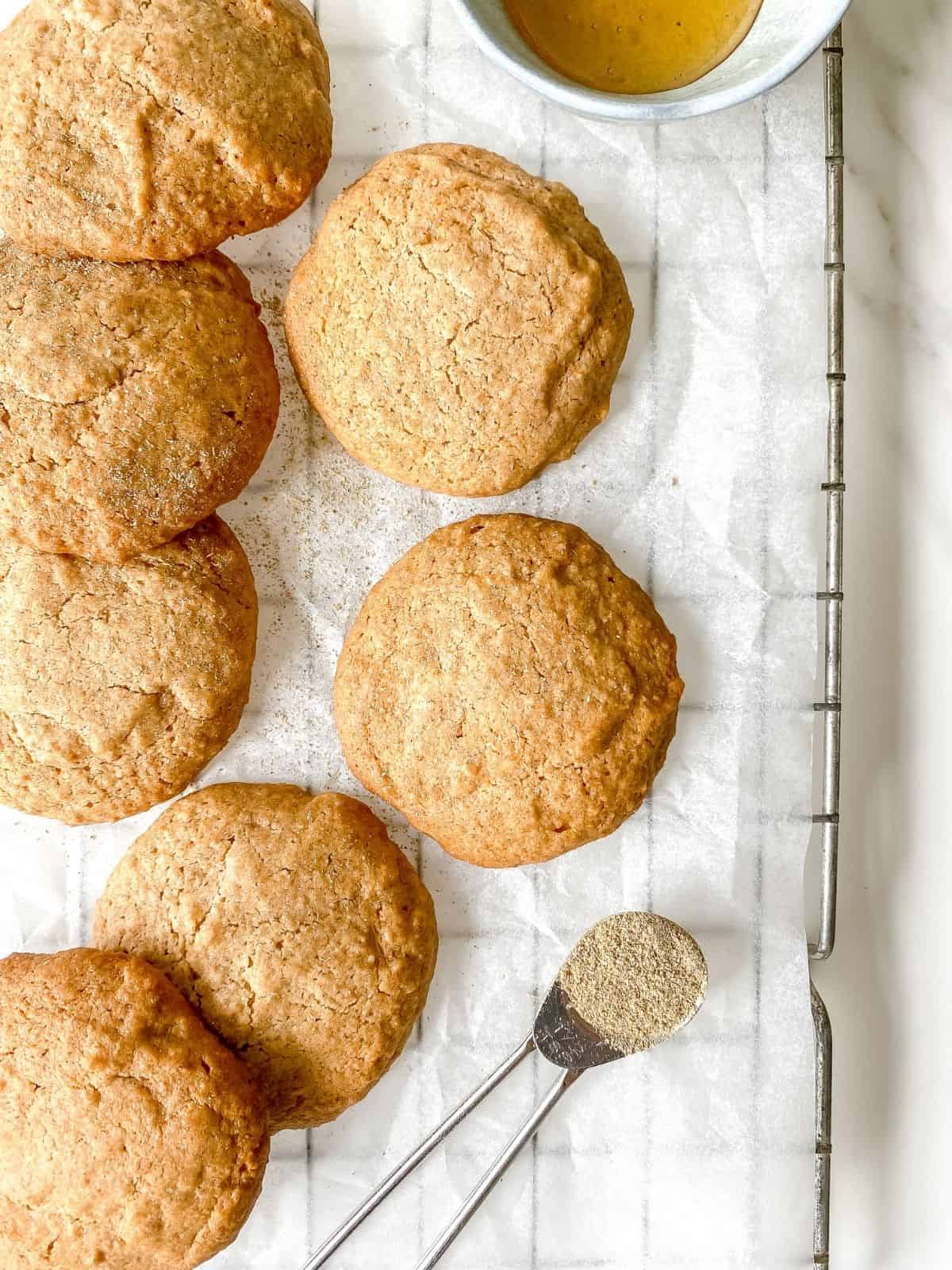 honey spelt cookies on a wire rack with a bowl of honey next to them.