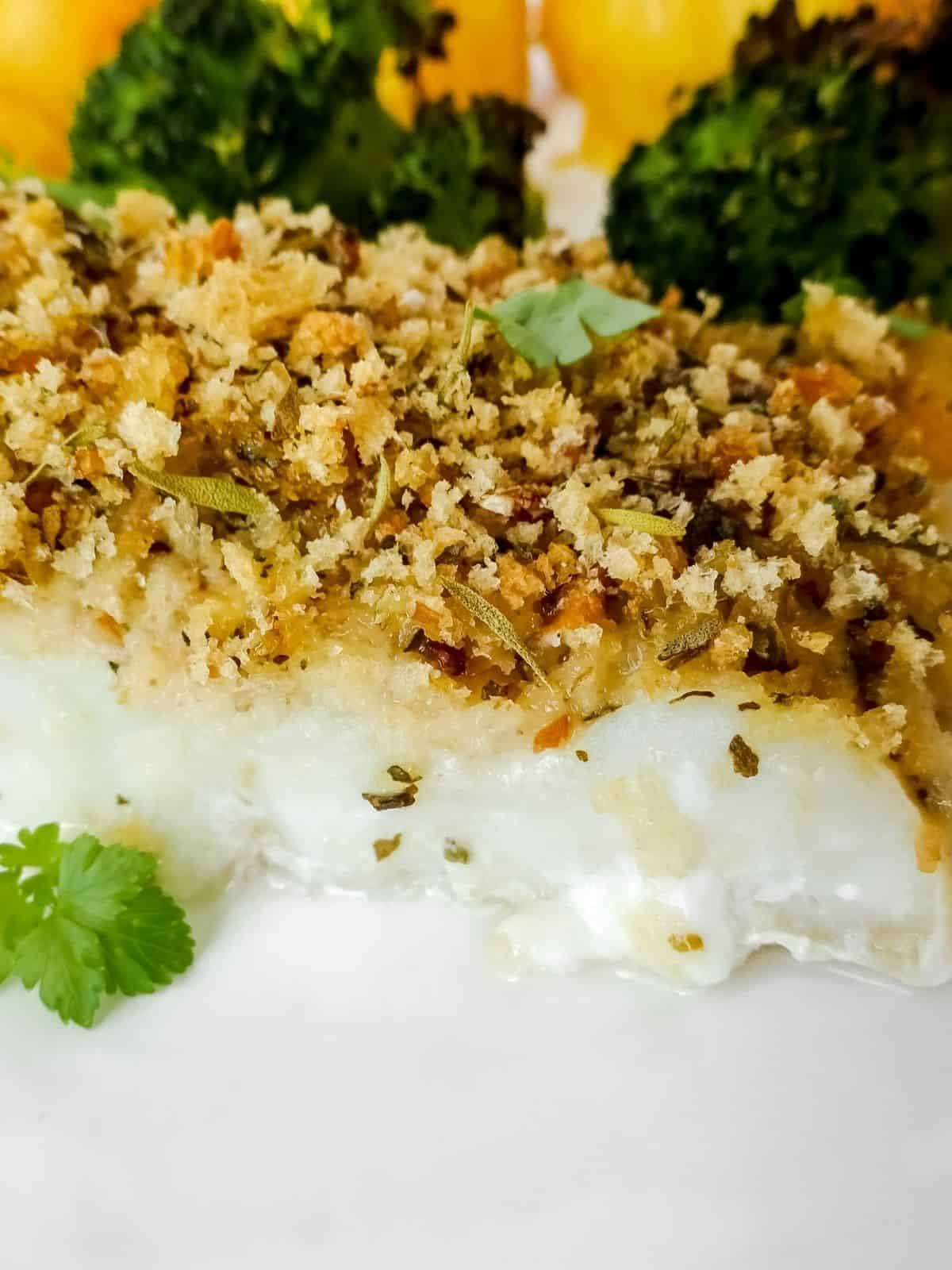 Close up of a piece of Italian herb crusted cod on a white plate.