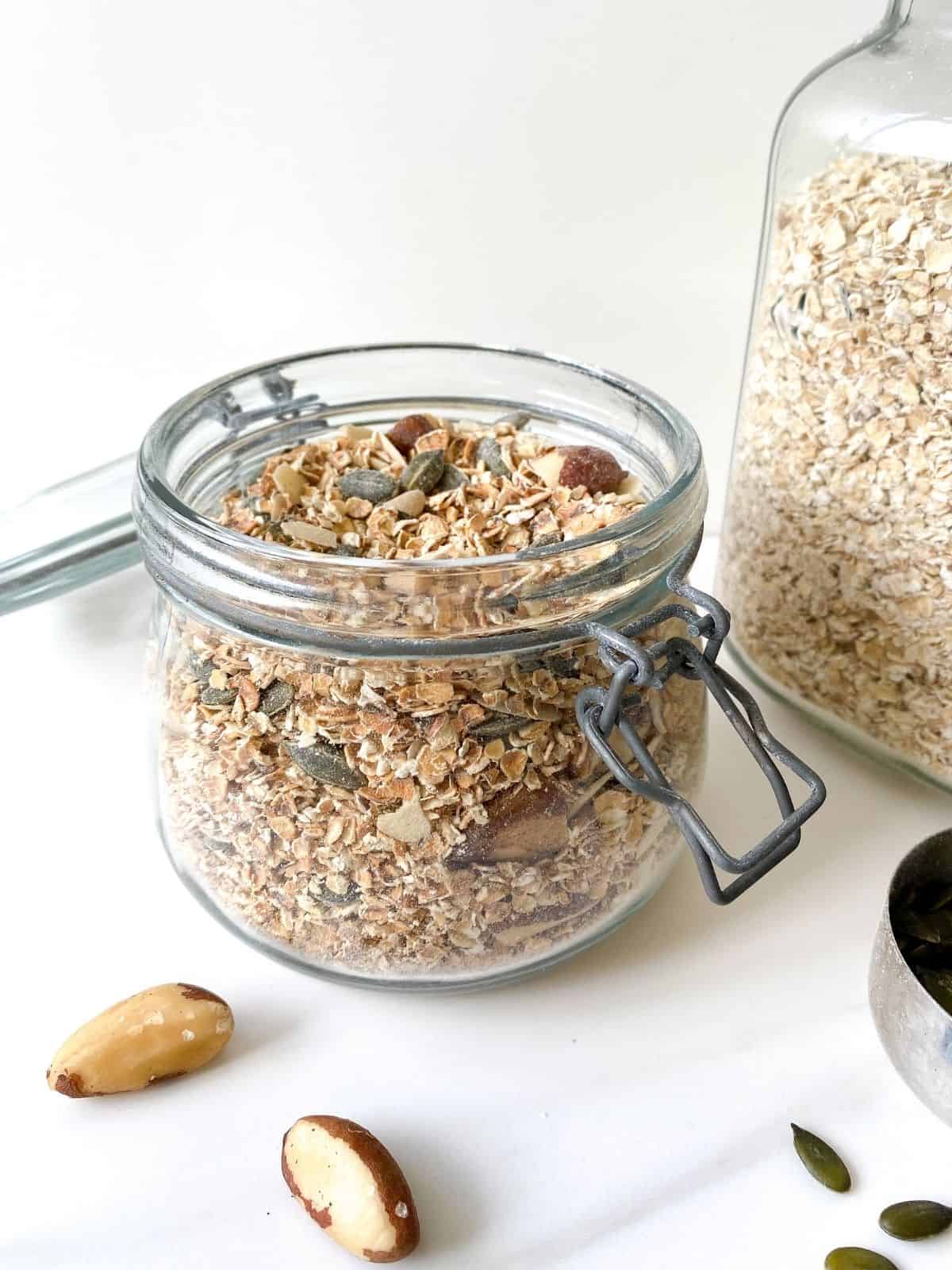 nut and seed muesli in a glass jar with a jar of oats in the background.
