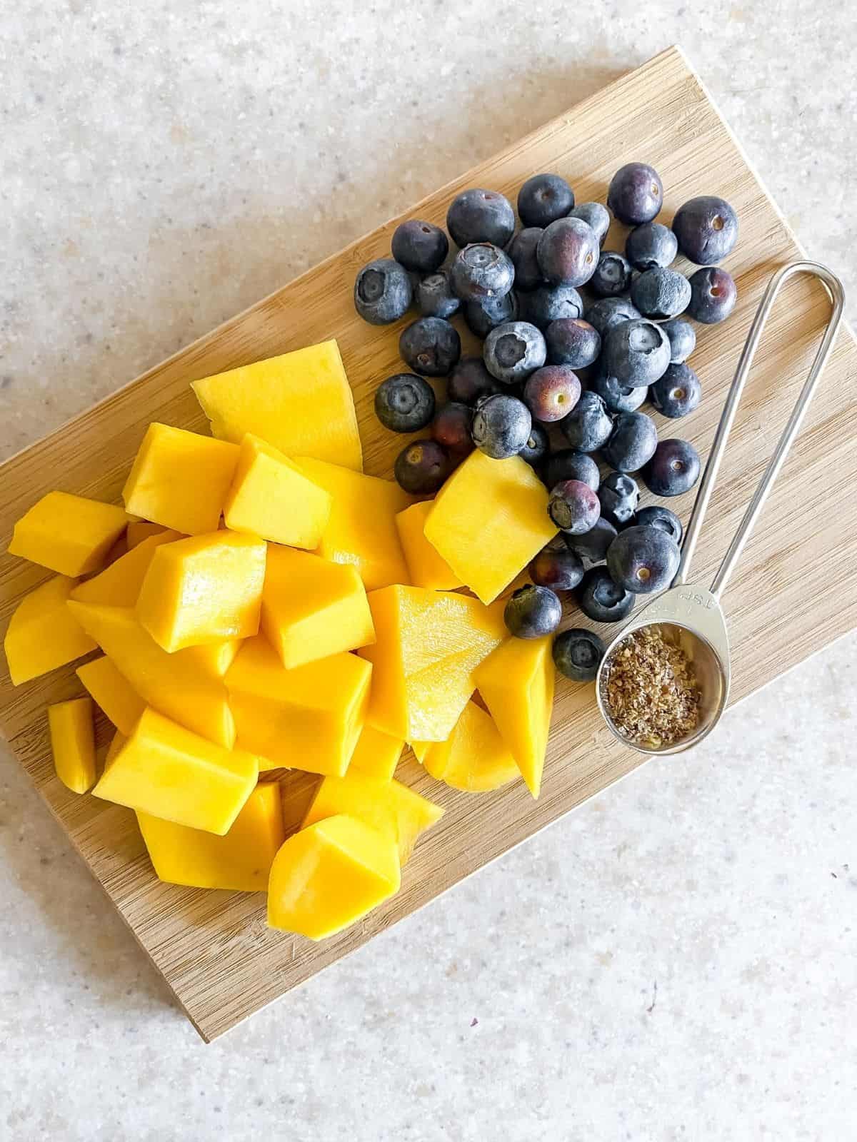 chopped mango and blueberries on a wooden chopping board.