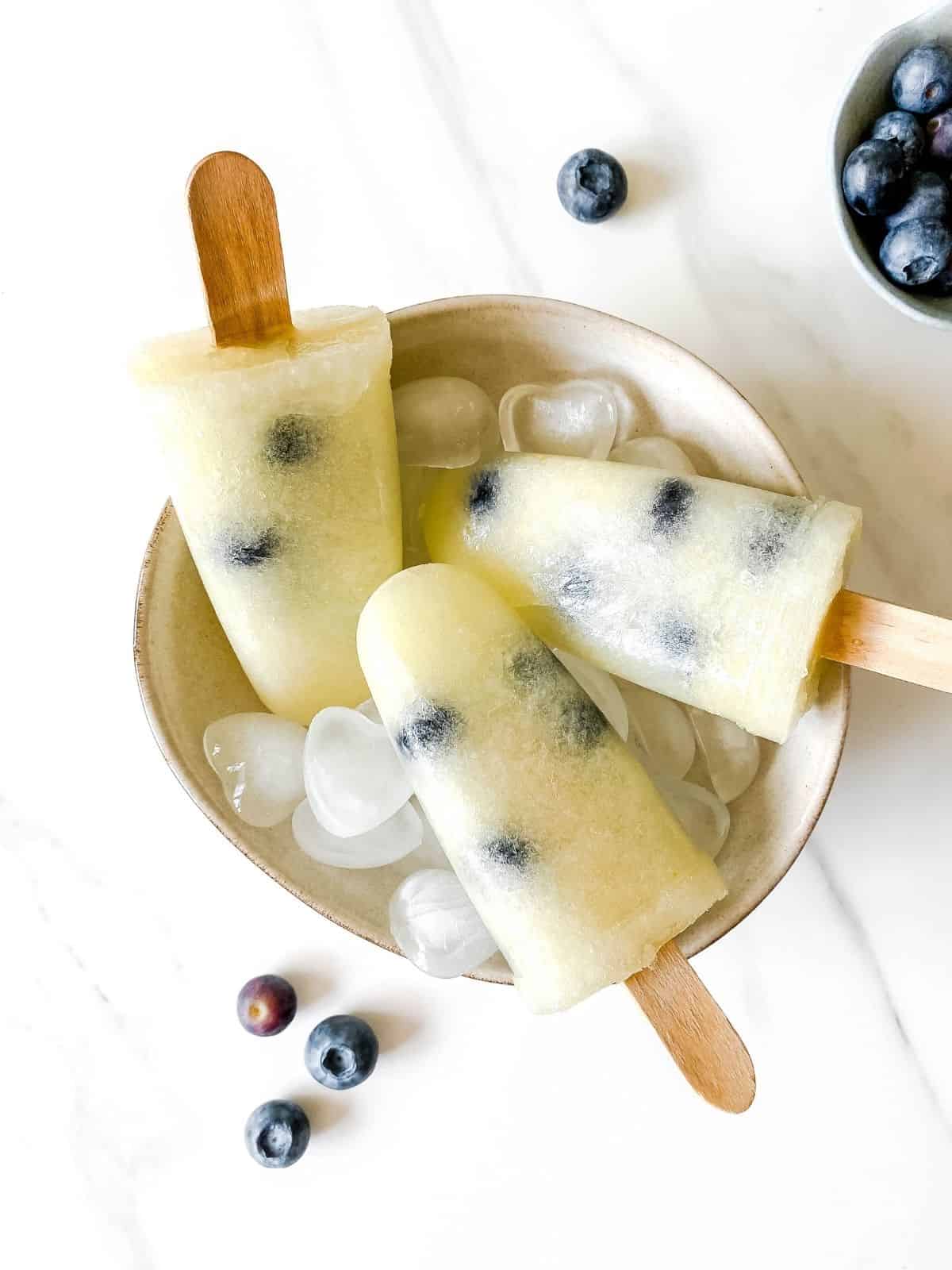 three honeydew melon blueberry popsicles in a bowl with ice in it.