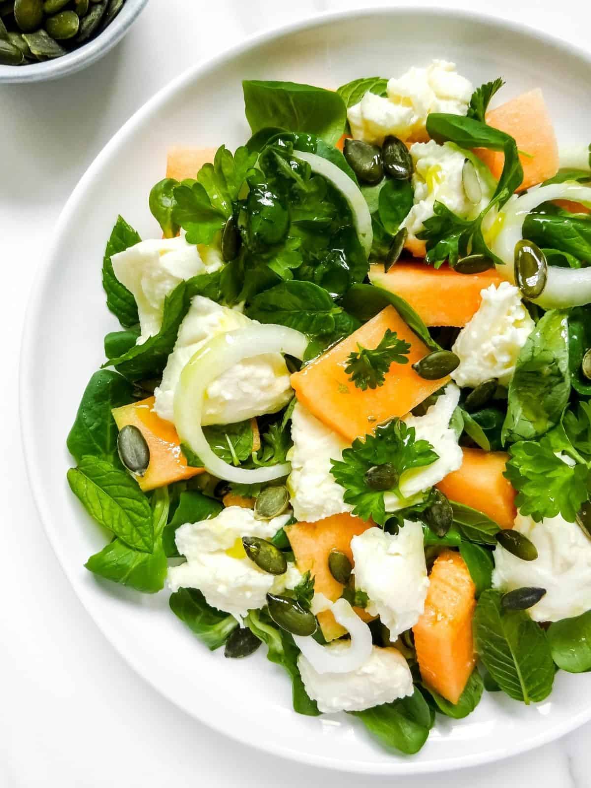 melon caprese salad on a white plate with a small bowl of pumpkin seeds next to it.