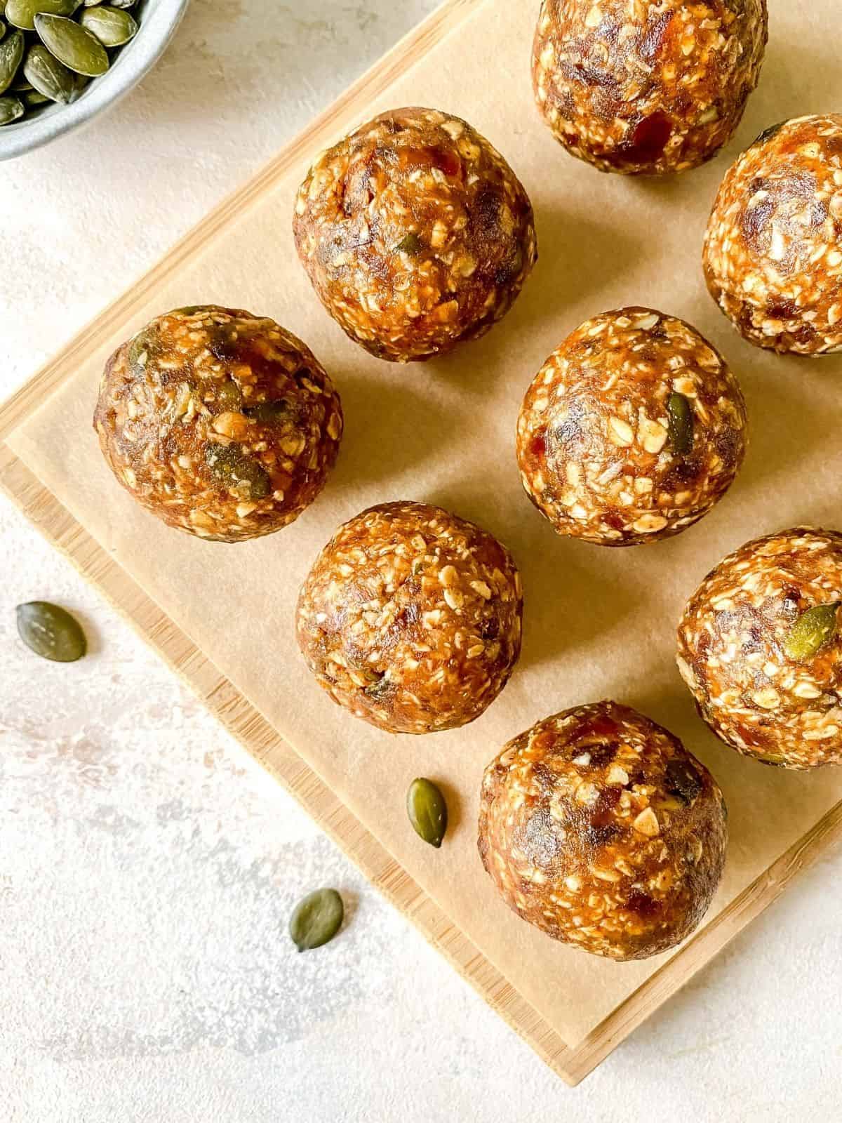 oatmeal bliss balls on a wooden board with a bowl of pumpkin seeds next to it.