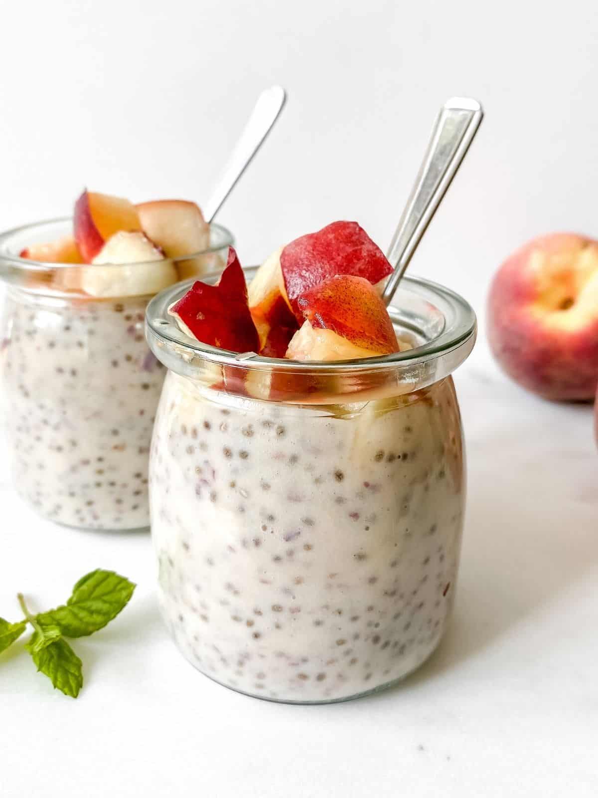 two glass jars of peach chia pudding with spoons in them.