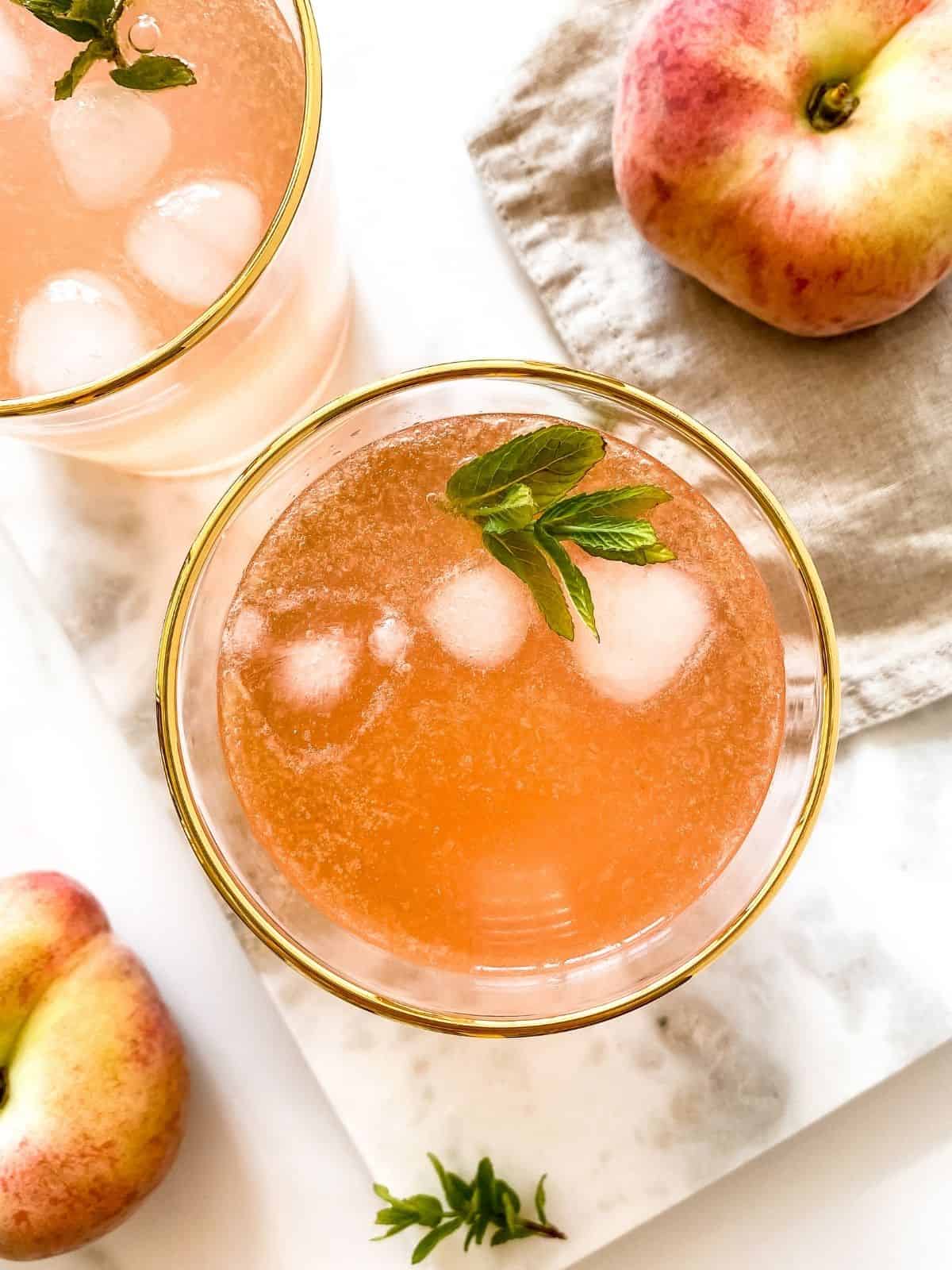 overhead view of two glasses of peach honey mocktail with peaches next to them.