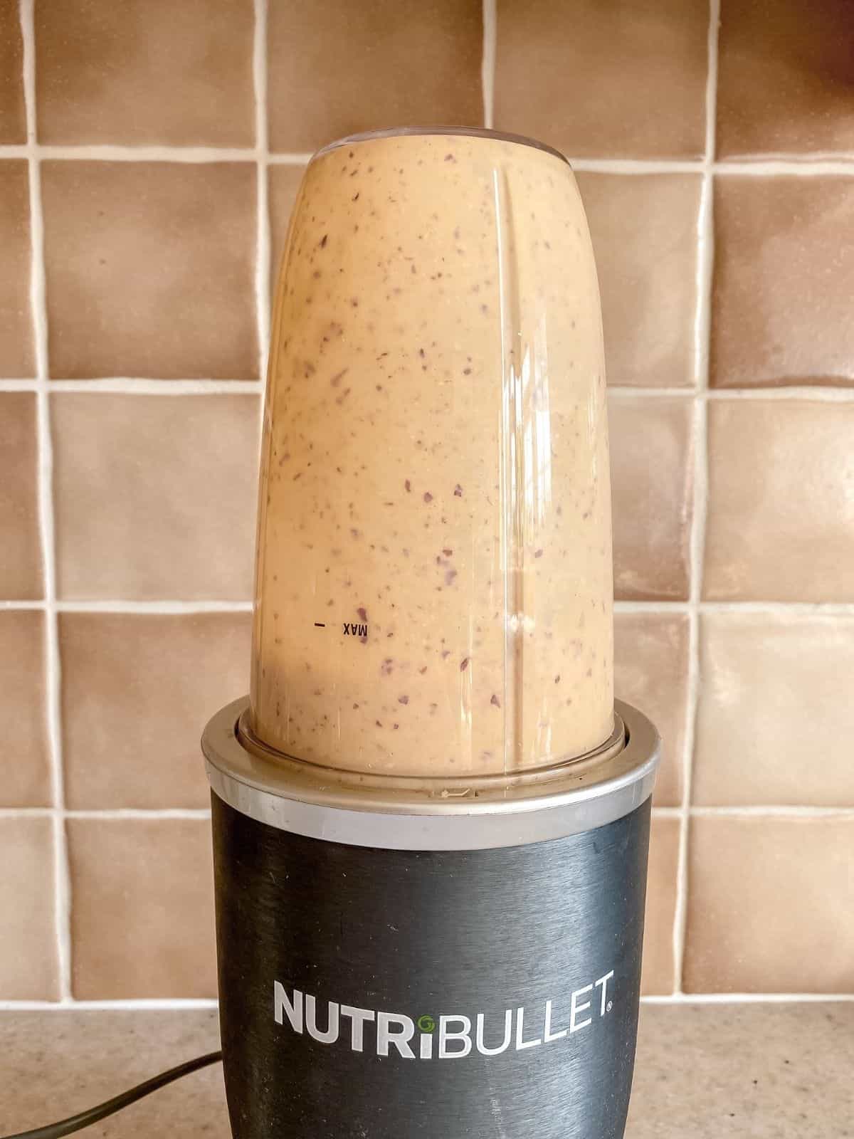 peach smoothie in a blender in front of a brown tiled wall.