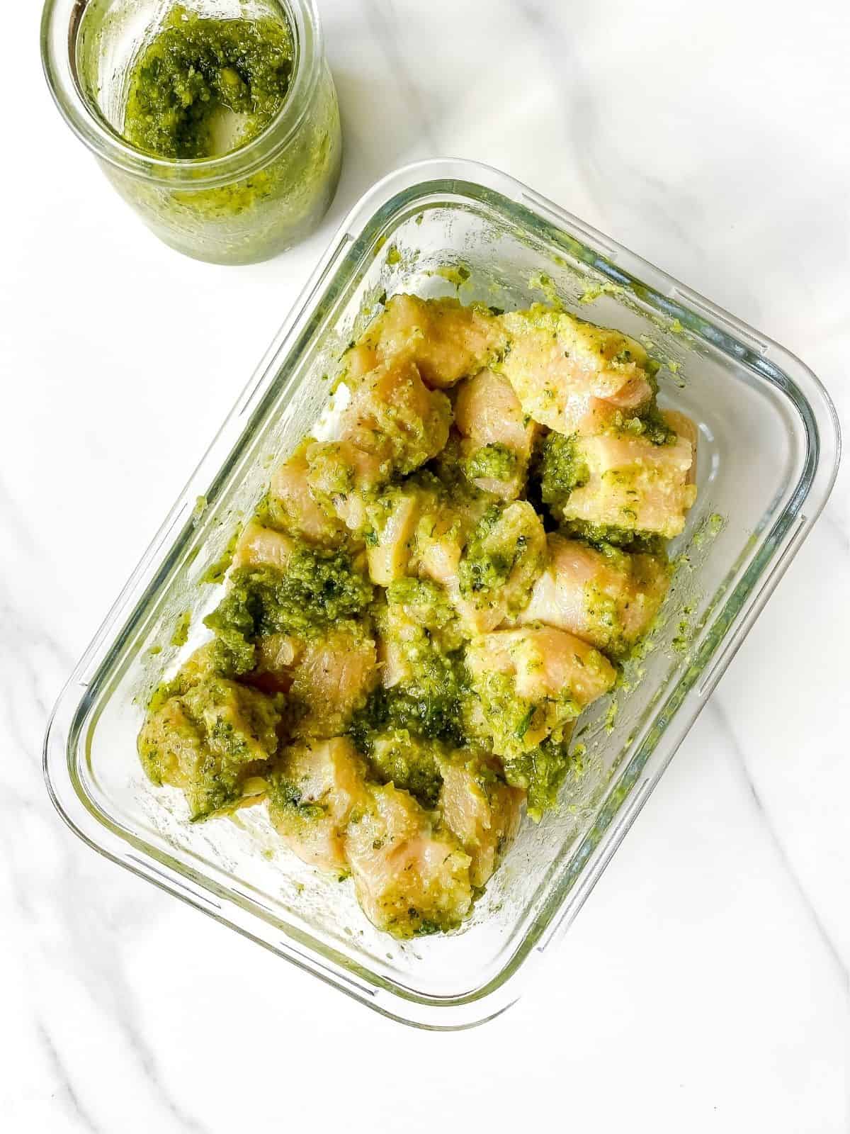 pesto coated chicken in a glass dish next to a jar of pesto.