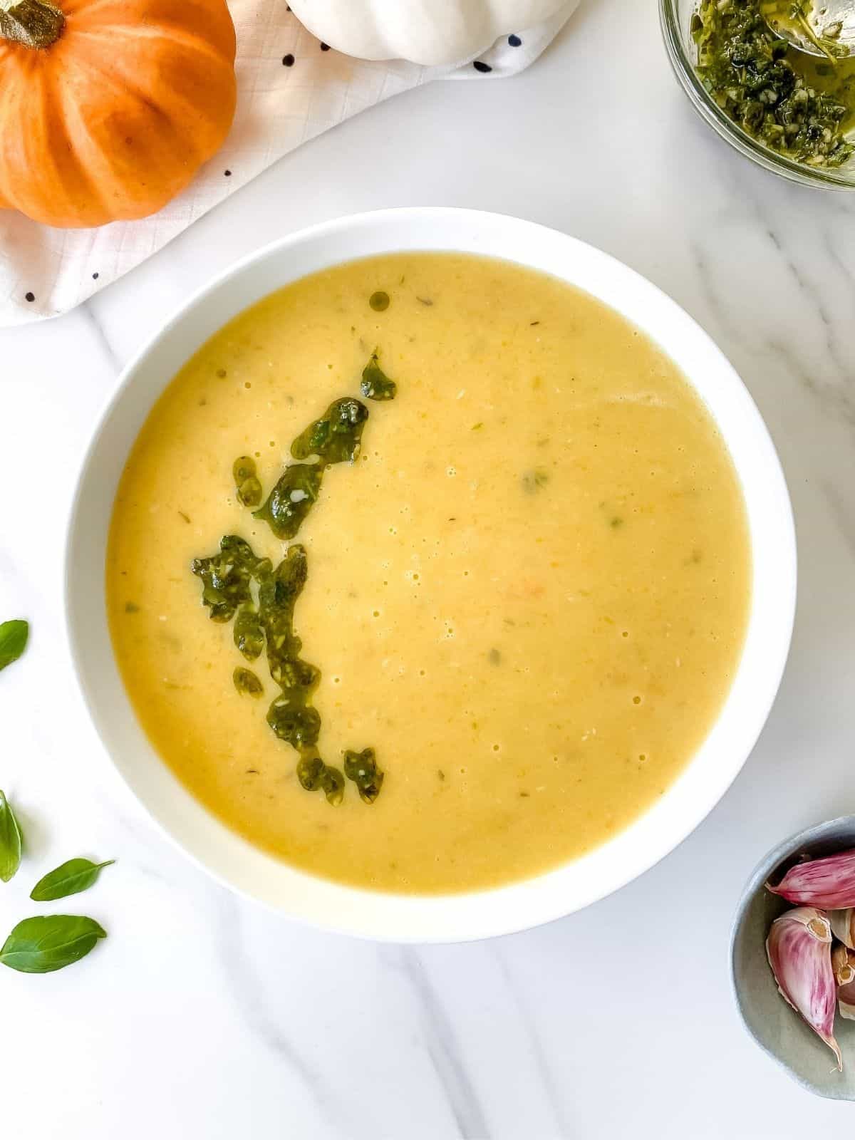 pumpkin pesto soup in a white bowl with pumpkins next to it.