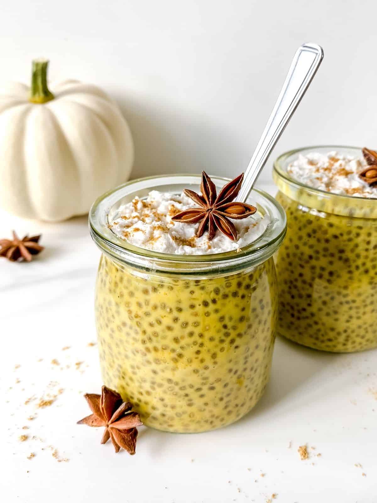 pumpkin spice chia pudding in glass jars with a white pumpkin in the background.