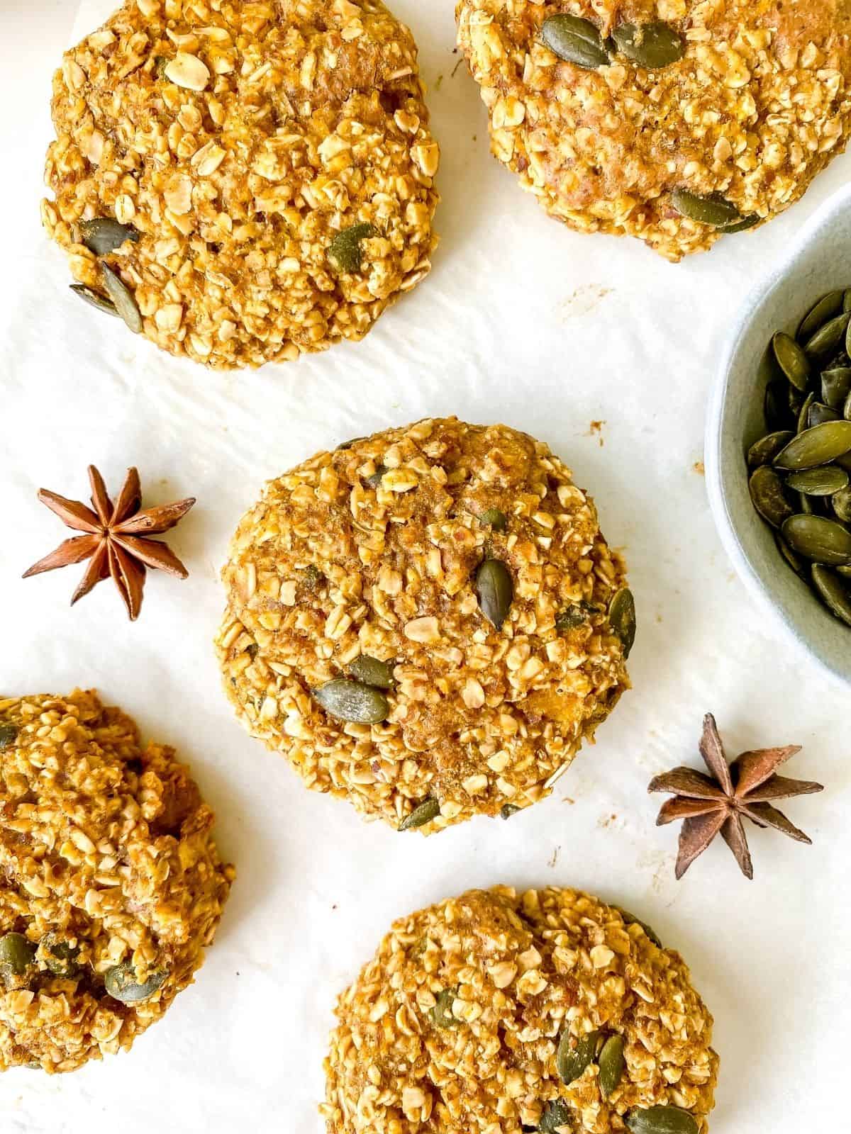 vegan pumpkin spice oatmeal cookies on a white background with star anise and pumpkin seeds next to them.