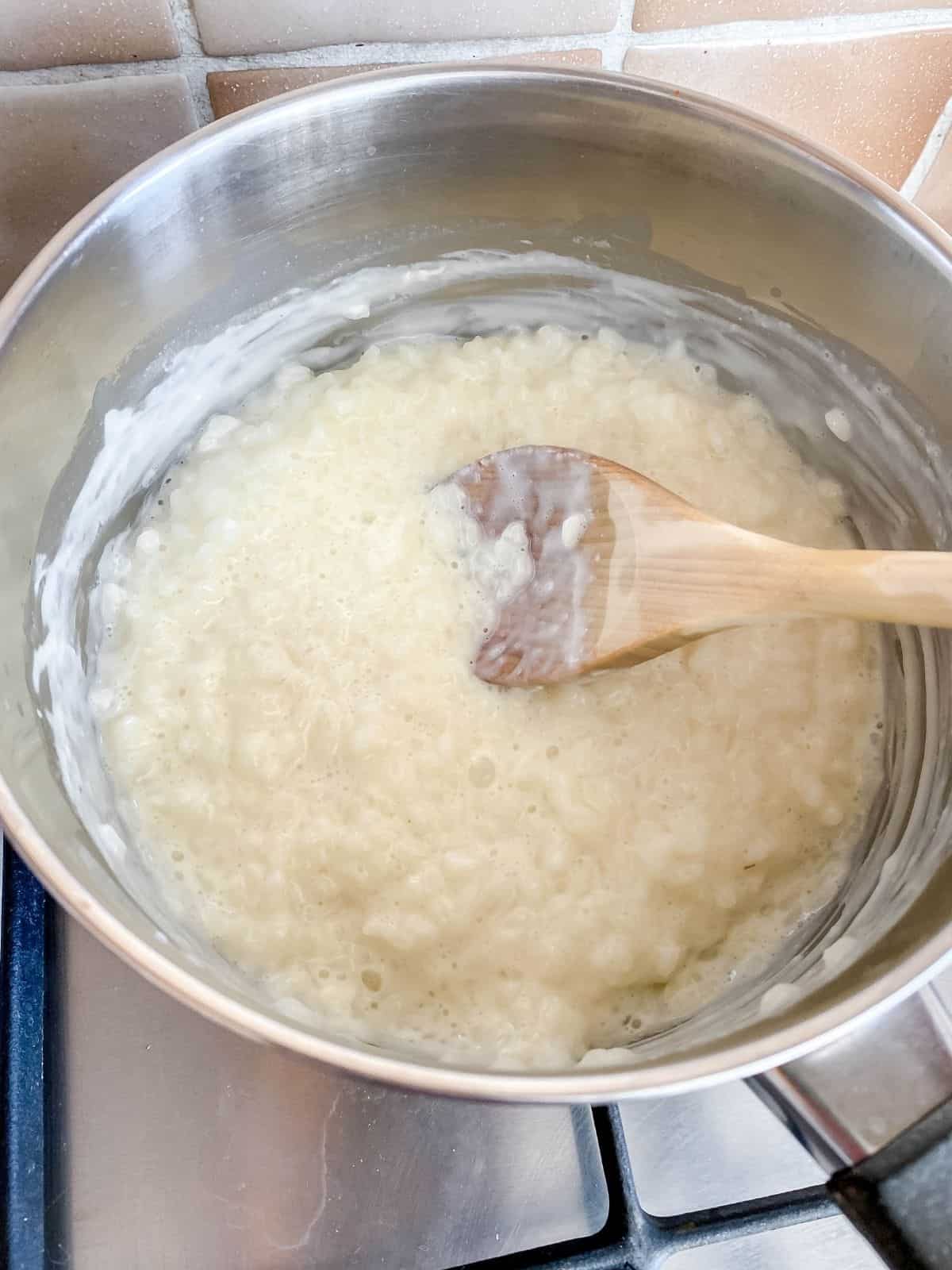 rice pudding in a pan being stirred with a wooden spoon.
