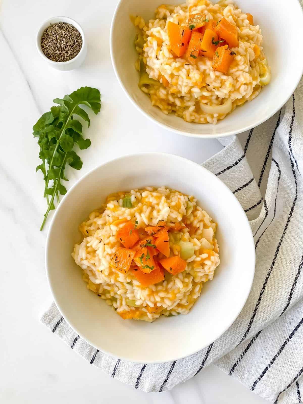 roasted butternut squash risotto in two white bowls on a striped cloth.