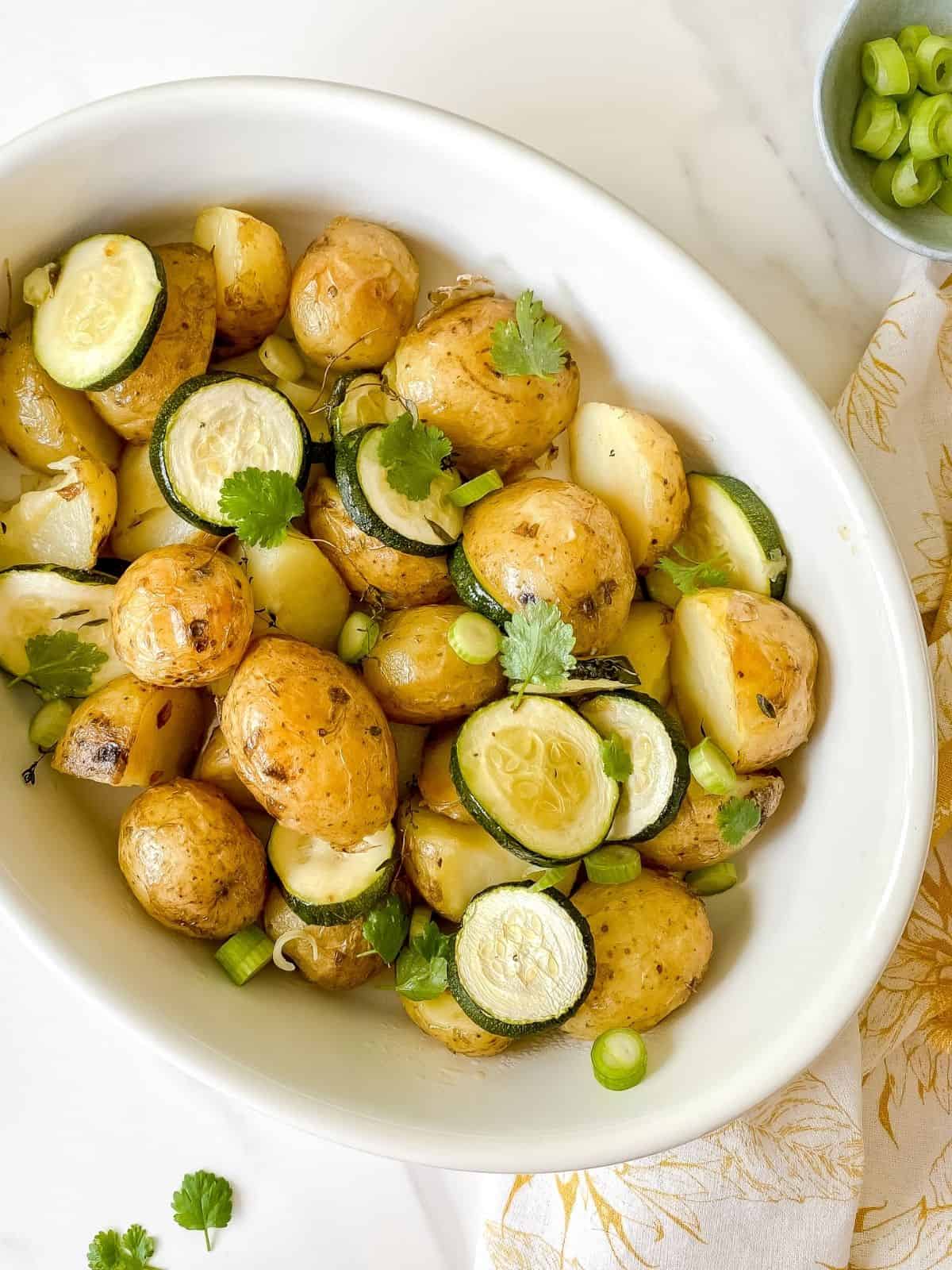 roasted potatoes and zucchini in a white dish on a patterned yellow cloth.