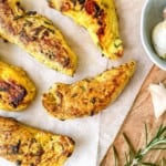 rosemary chicken fillets next to garlic and a sprig of rosemary on a wooden board.