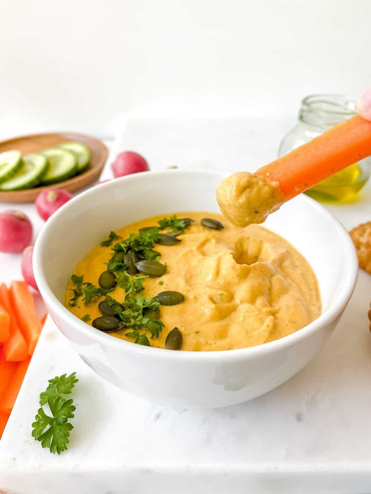 spicy zucchini baba ganoush with someone dipping a carrot stick into the bowl.